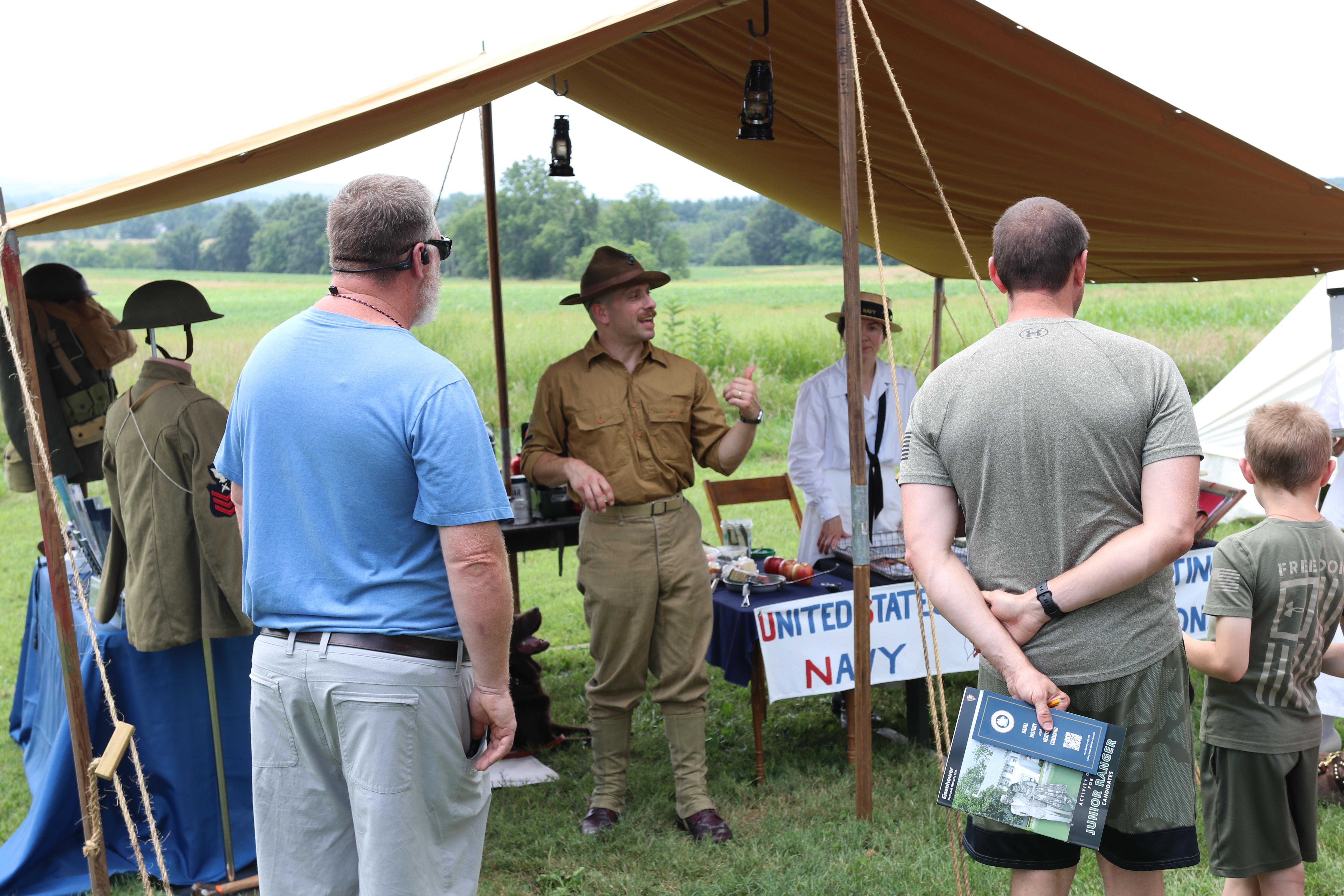 A living history volunteer speaks with visitors under a brown tent