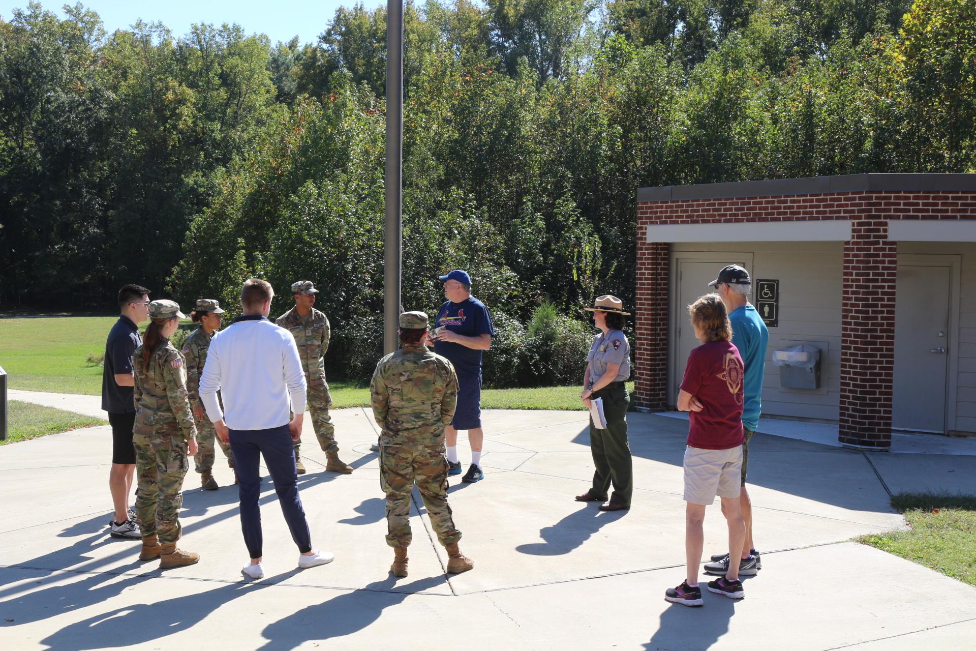 A Park Ranger and a group of 9 people both civilian and military in a circle around a flagpole.
