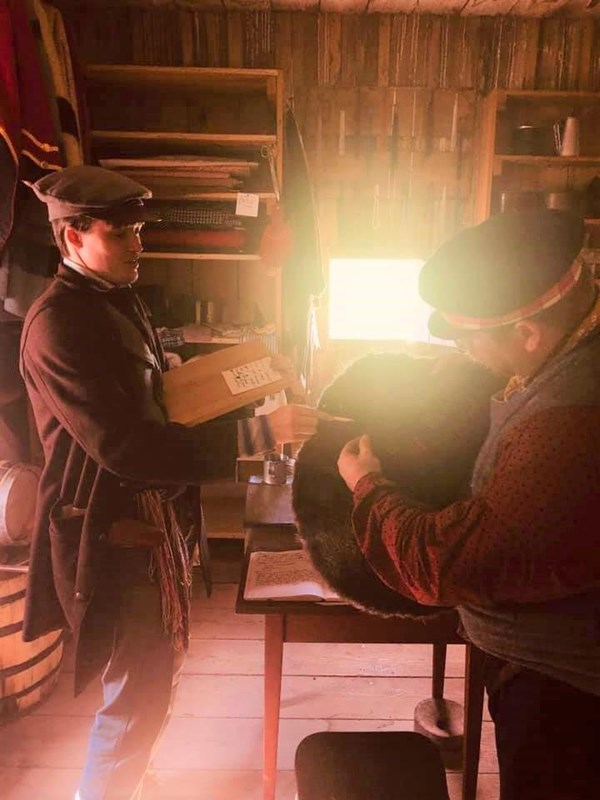 Two men stand in shop examining a beaver plew or hide.