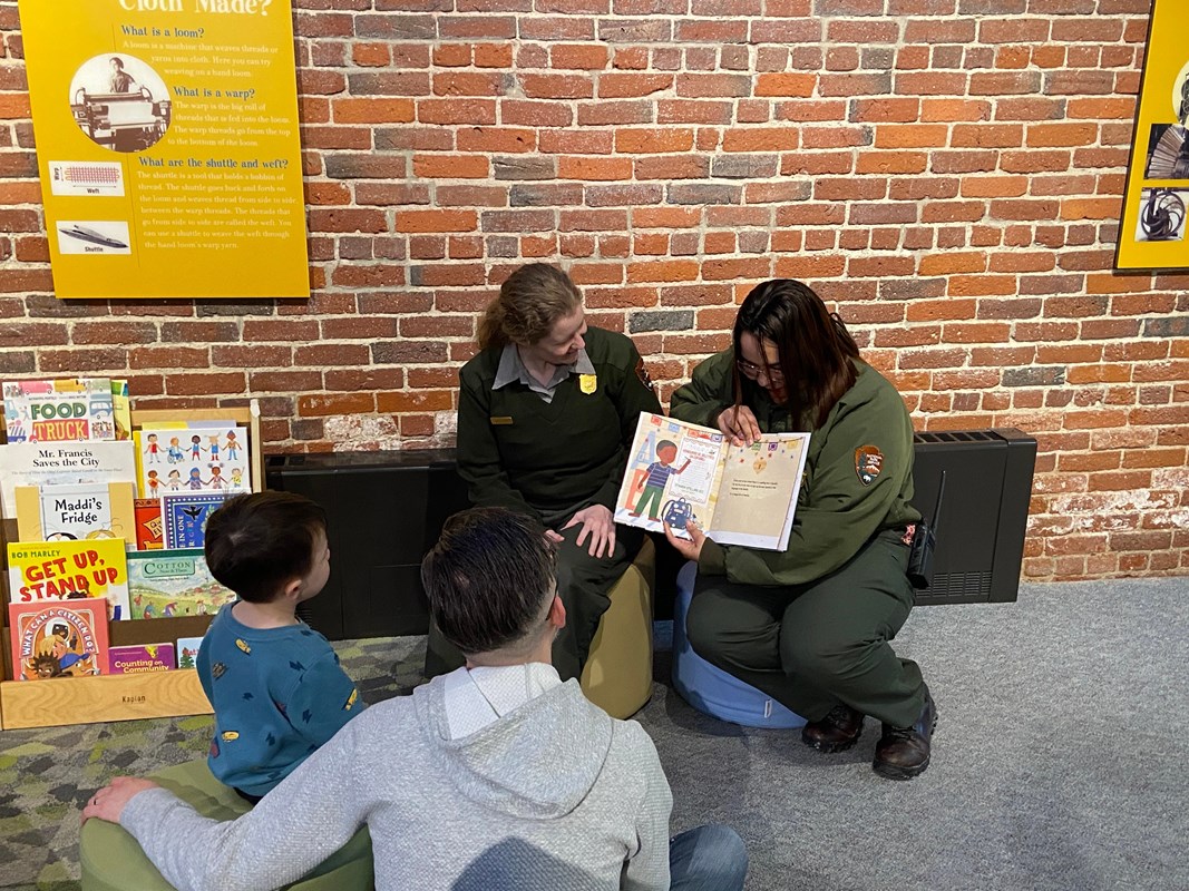 Two rangers read a picture book to a small child and parent.
