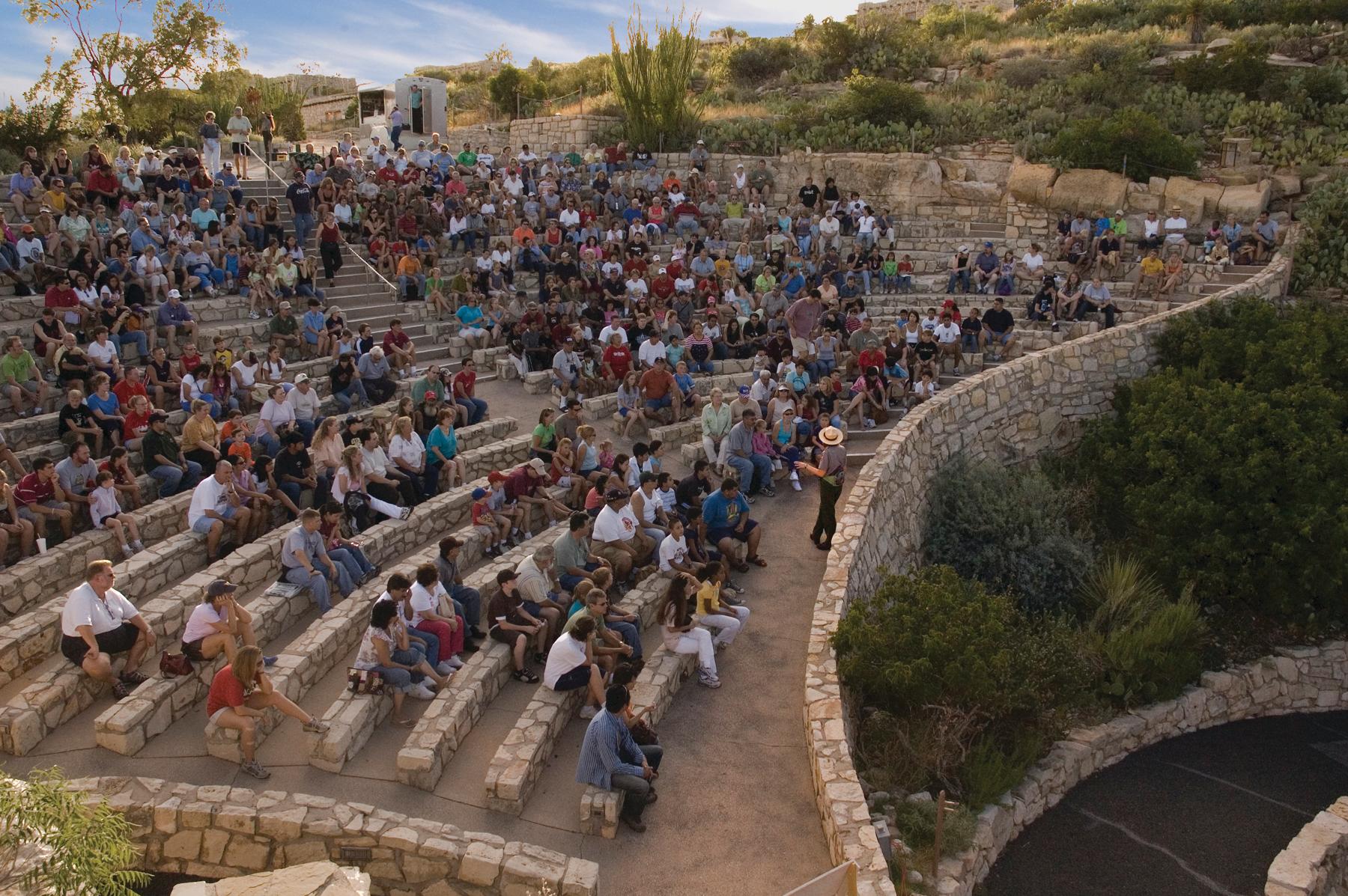 a picture of visitors sitting in the amphitheater listening to a park ranger's program