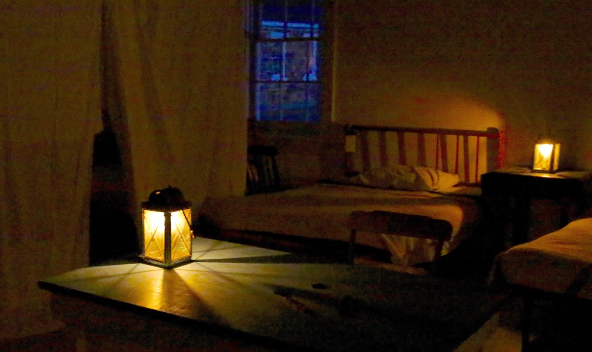 Dark room with candle lantern on a table next to a hospital bed.