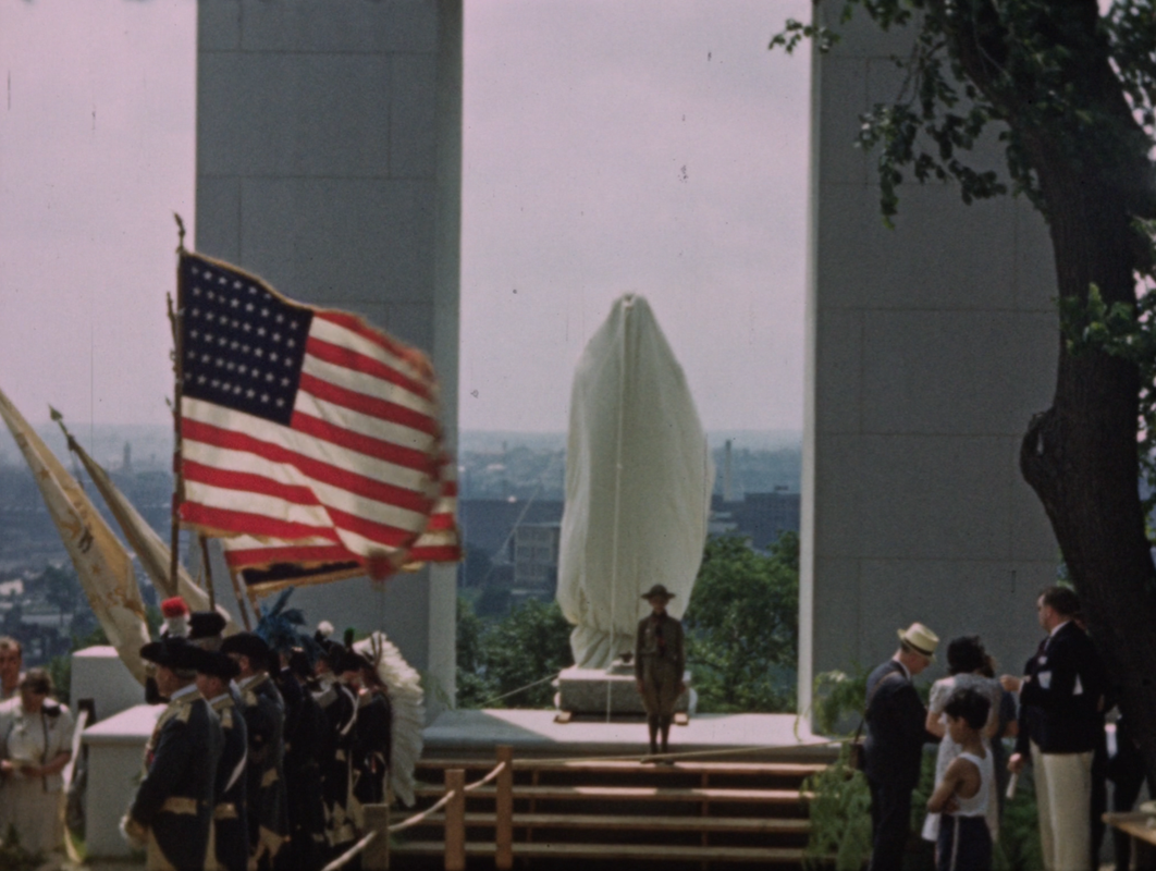 Group of people around covered monument with American flag and reenactors in the foreground