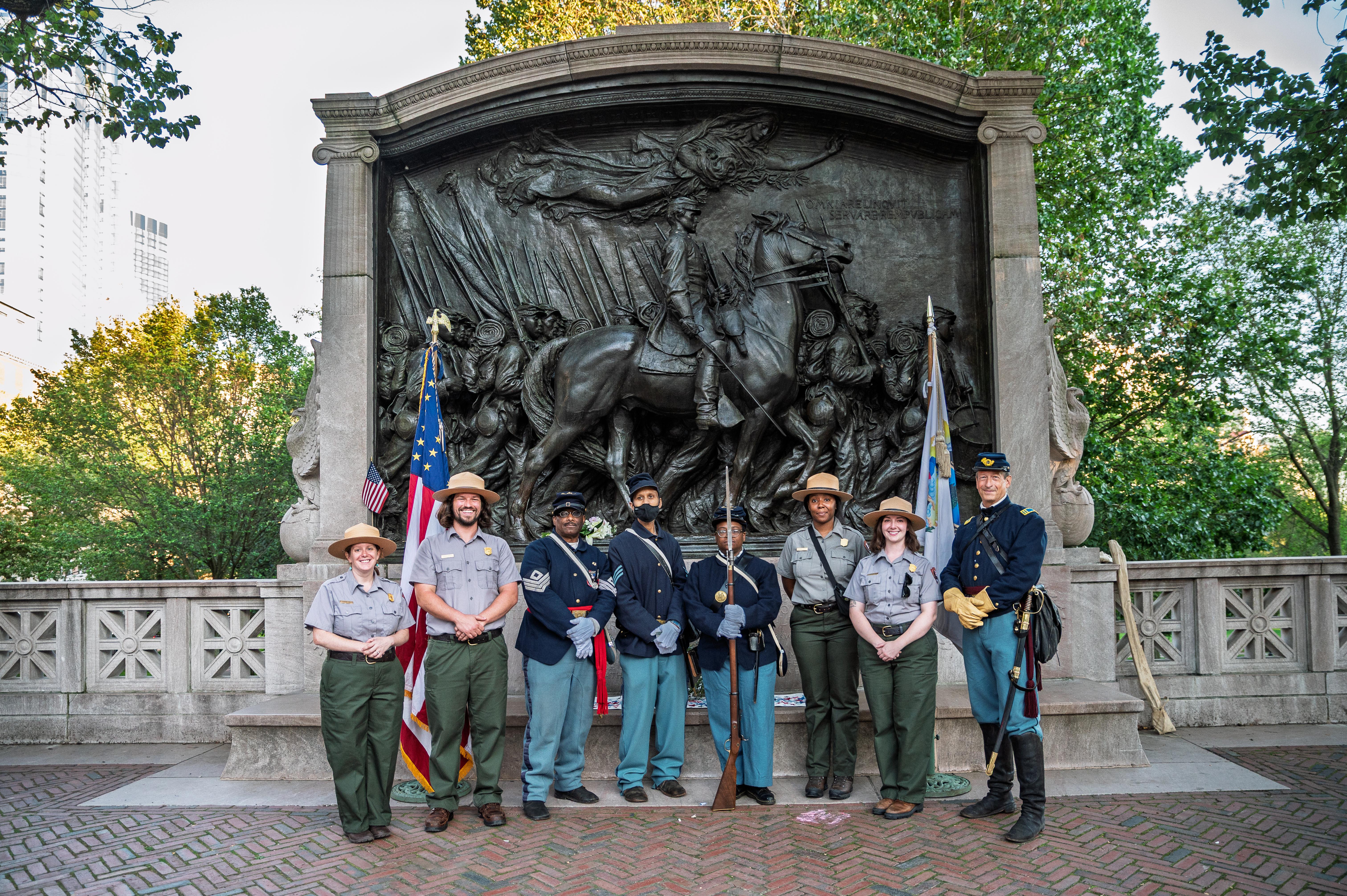 Rangers in uniform stand with people in historic military dress in front of the Shaw/54th monument