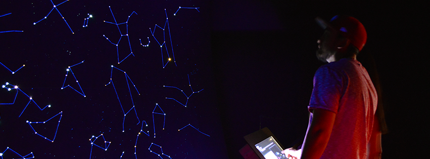 A man looks at a dark screen, with bright lights; images of constellations.
