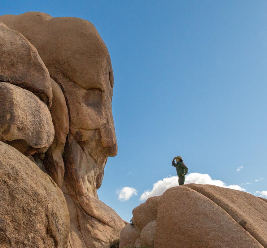 A ranger looks towards a rock that resembles human face