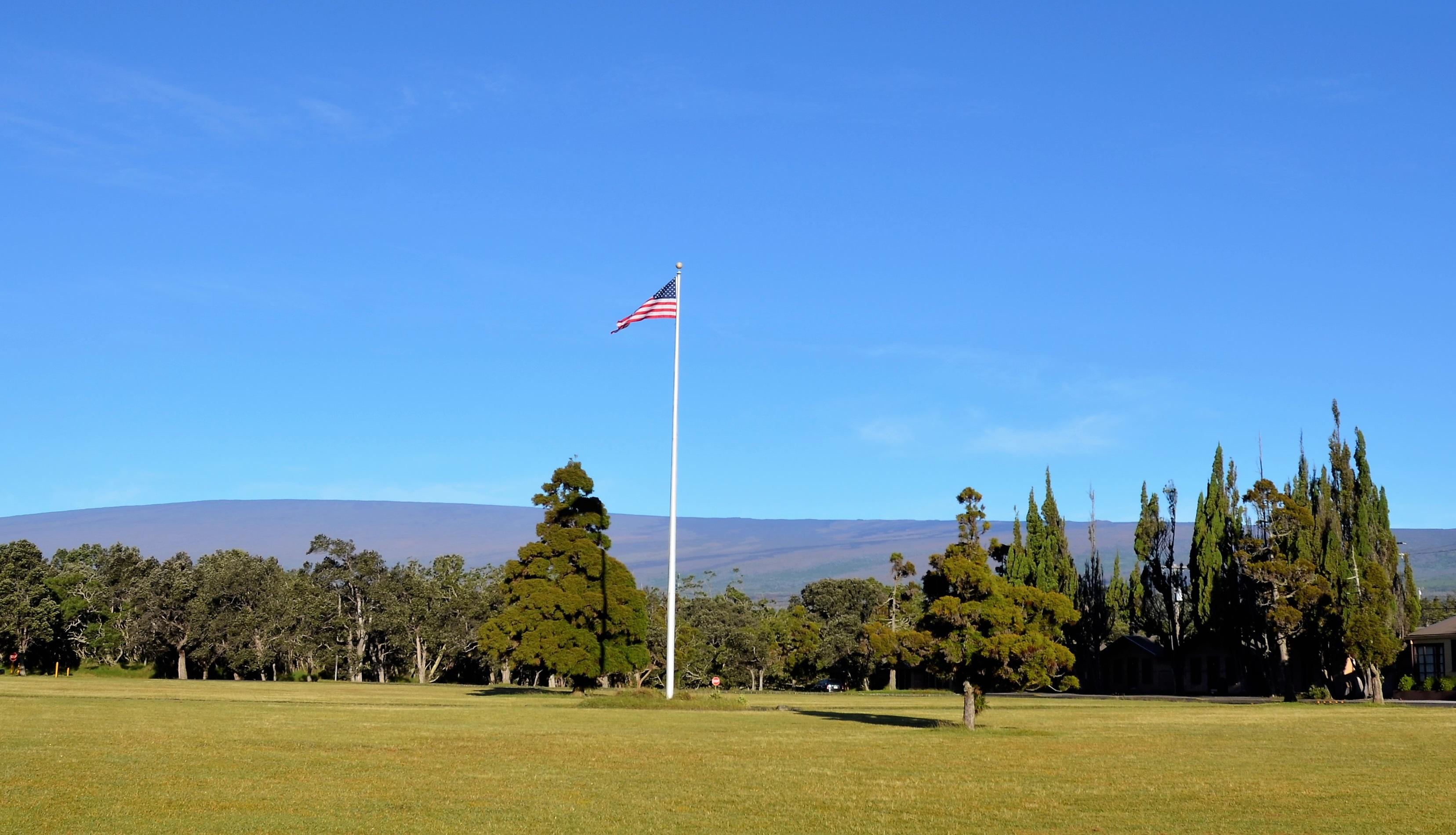 The American flag flies high on a tall staff in the middle of a grassy field