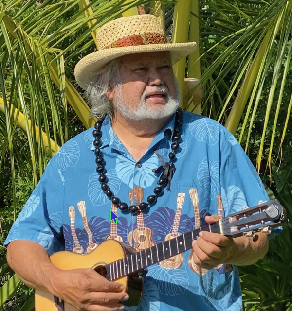 Profile of a man in an aloha shirt, straw hat and lei playing the ʻukulele stringed instrument