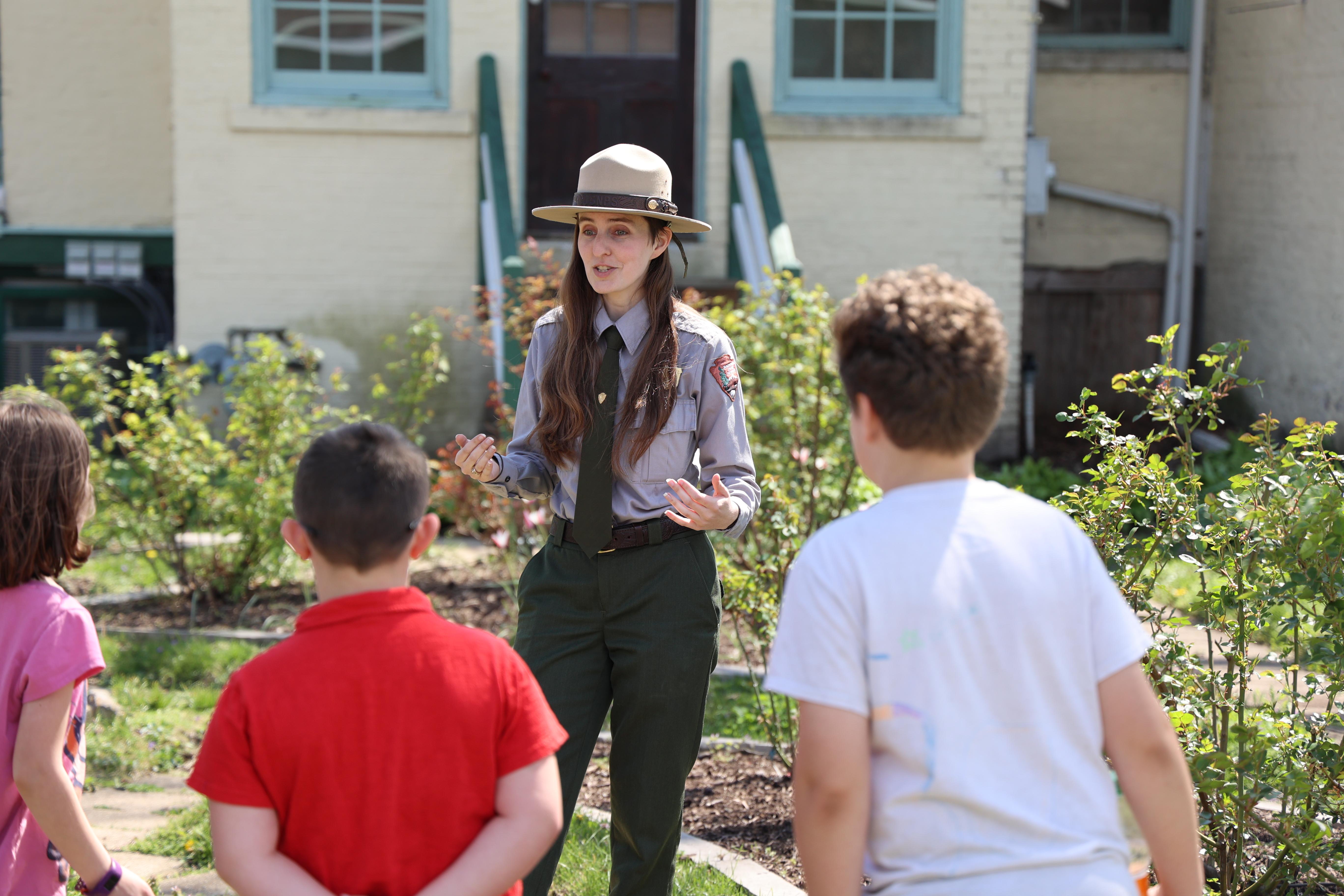 Park Ranger talks to students in a rose garden next to a historic house.