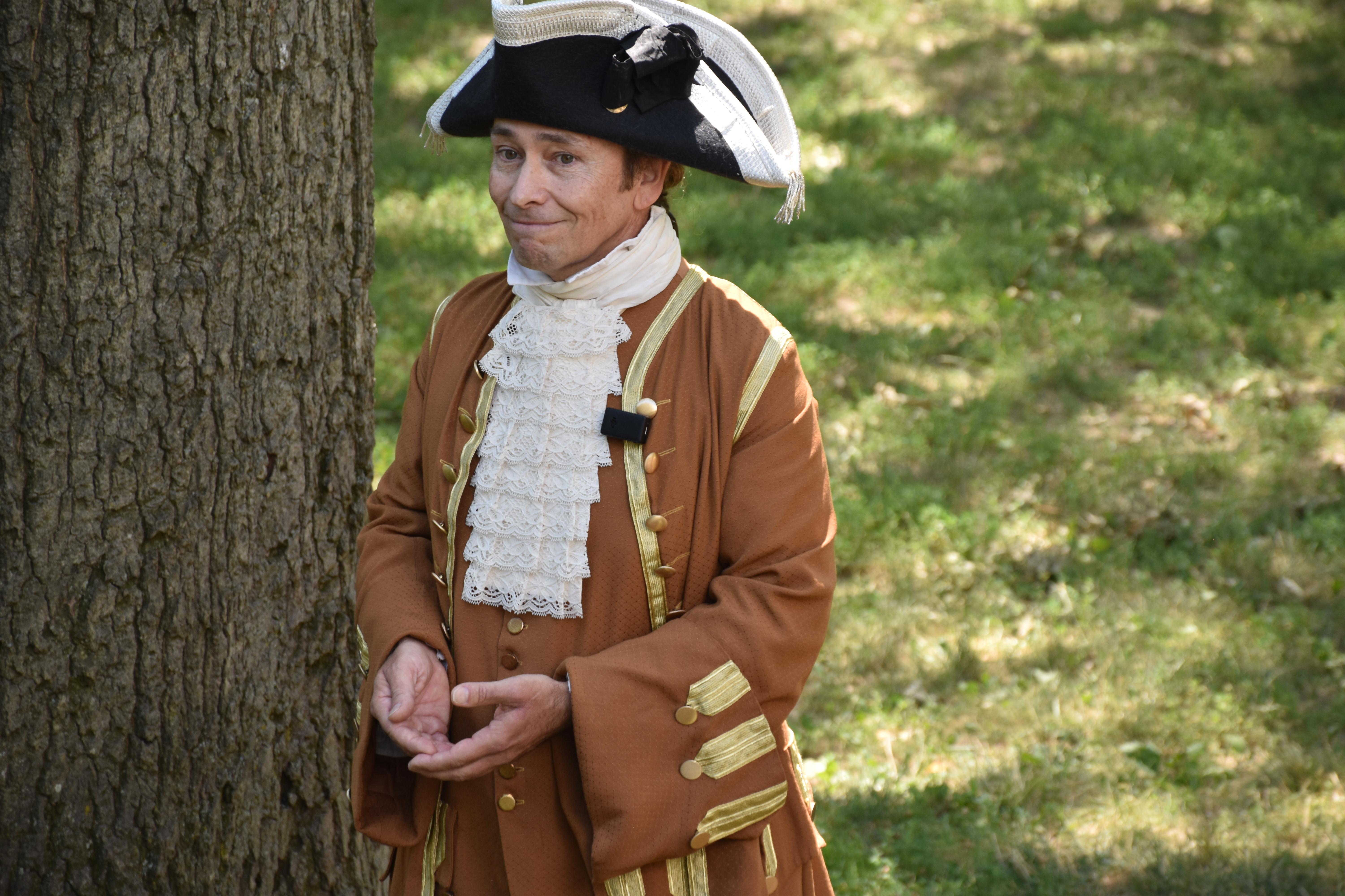 A man dressed in colonial period clothing in a grassy lawn.