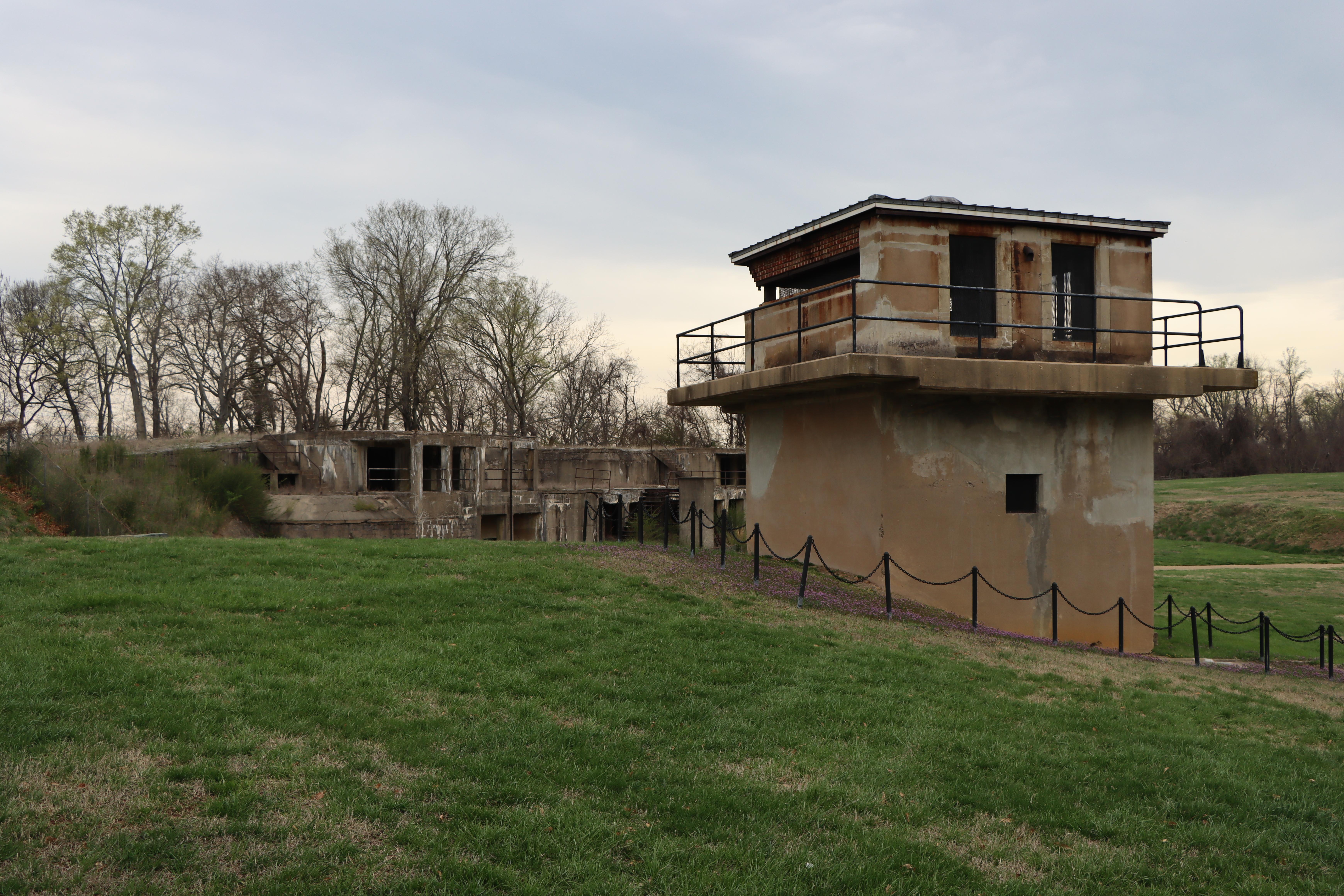 A tan cement building with an old cement battery in the background.