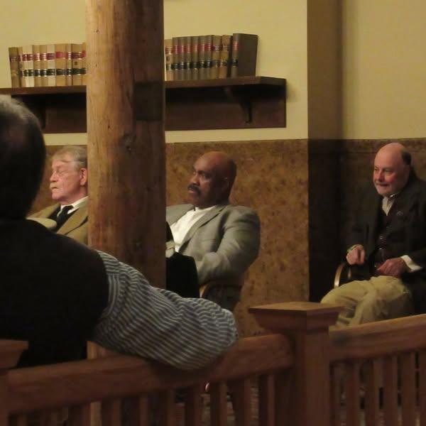 Three men dressed in historic clothing sitting in historic courtroom during a mock trial.