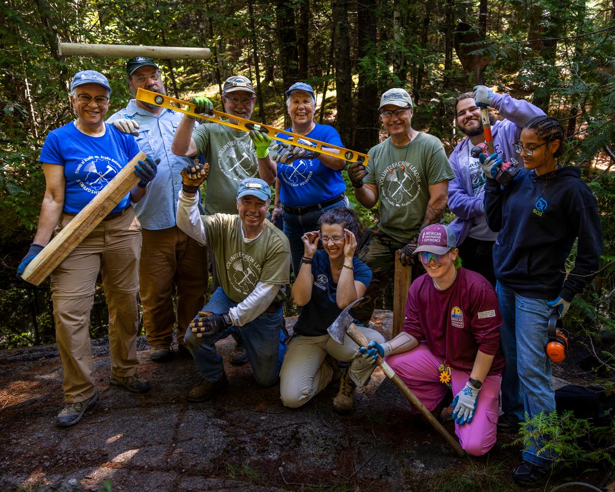 Group photo of 10 people in a wooded setting holding forestry and landscaping tools