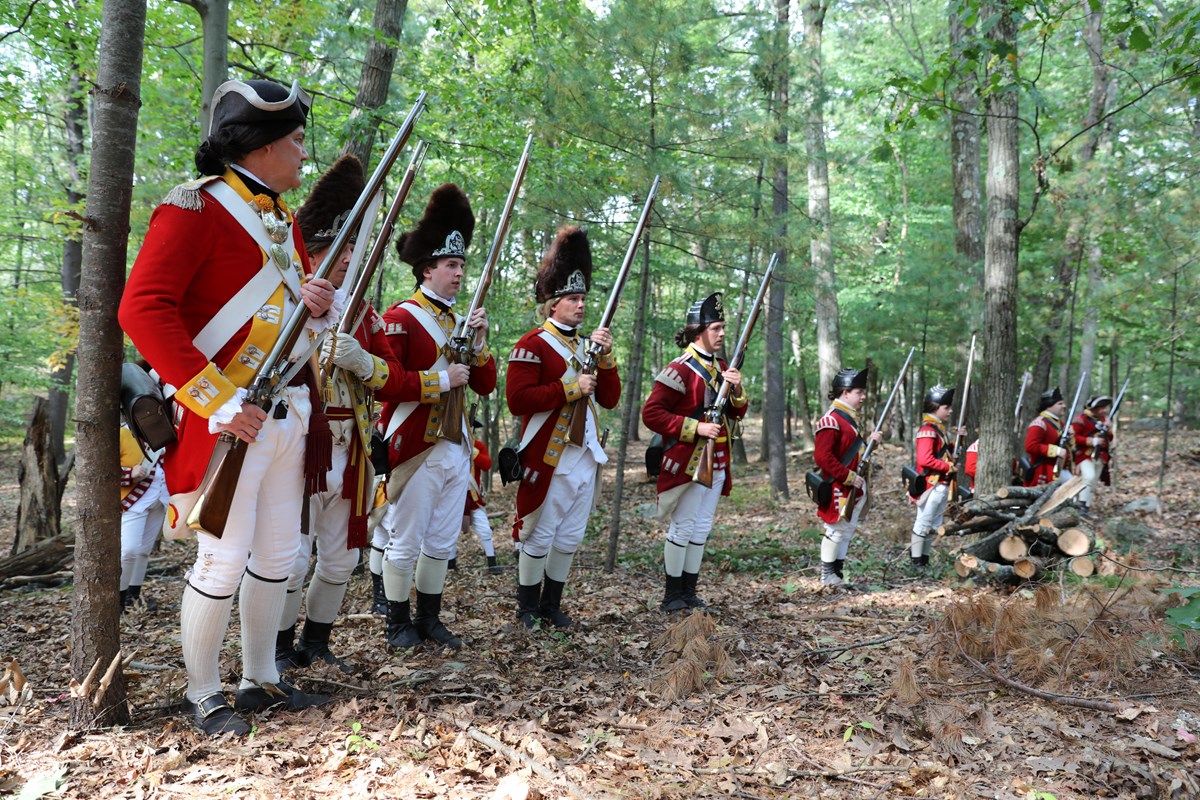 Revolutionary War British soldiers in red uniforms line up in a wooded area