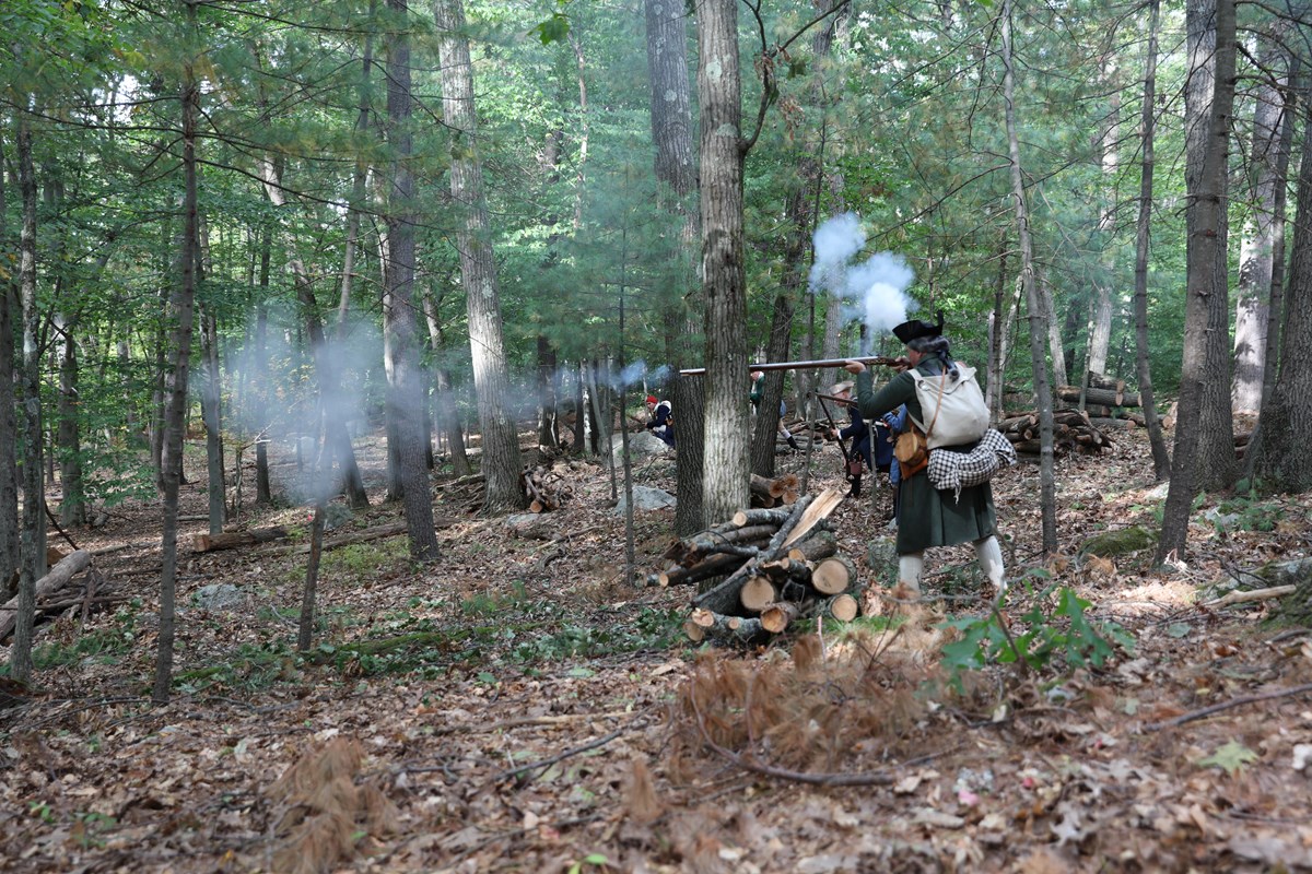 Revolutionary War Colonial soldiers fire their muskets in a wooded area.
