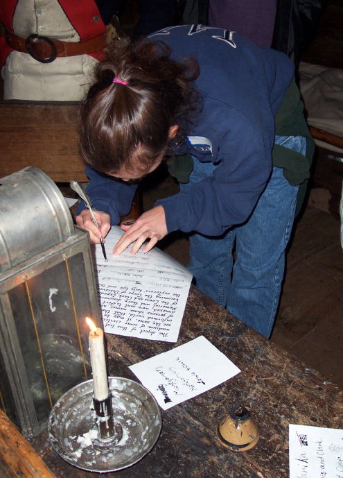 Woman writes on a large piece of paper by candlelight with a quill pen.