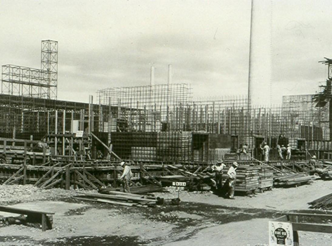 Historic photo of 6 construction workers at a worksite filled with a  half-build concrete structure.