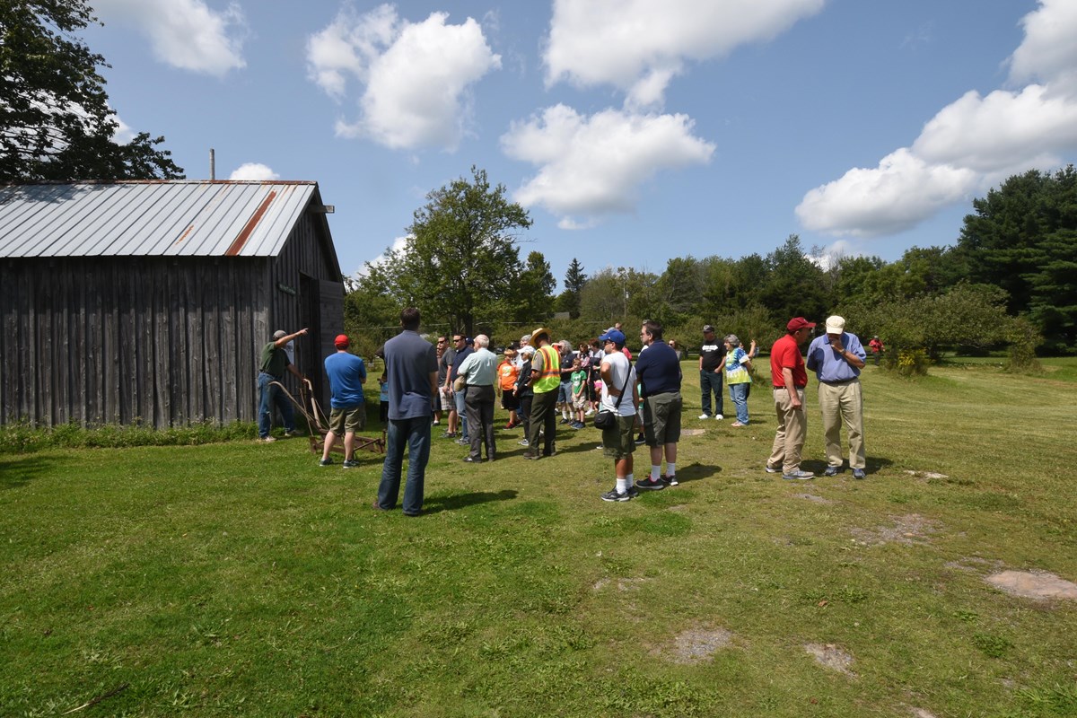 A crowd of approximately 30 people gathered outdoors in front of historic ice house