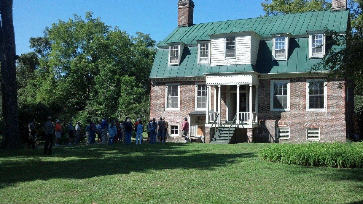 A group of visitors are gathered in front of an historic brick mansion.