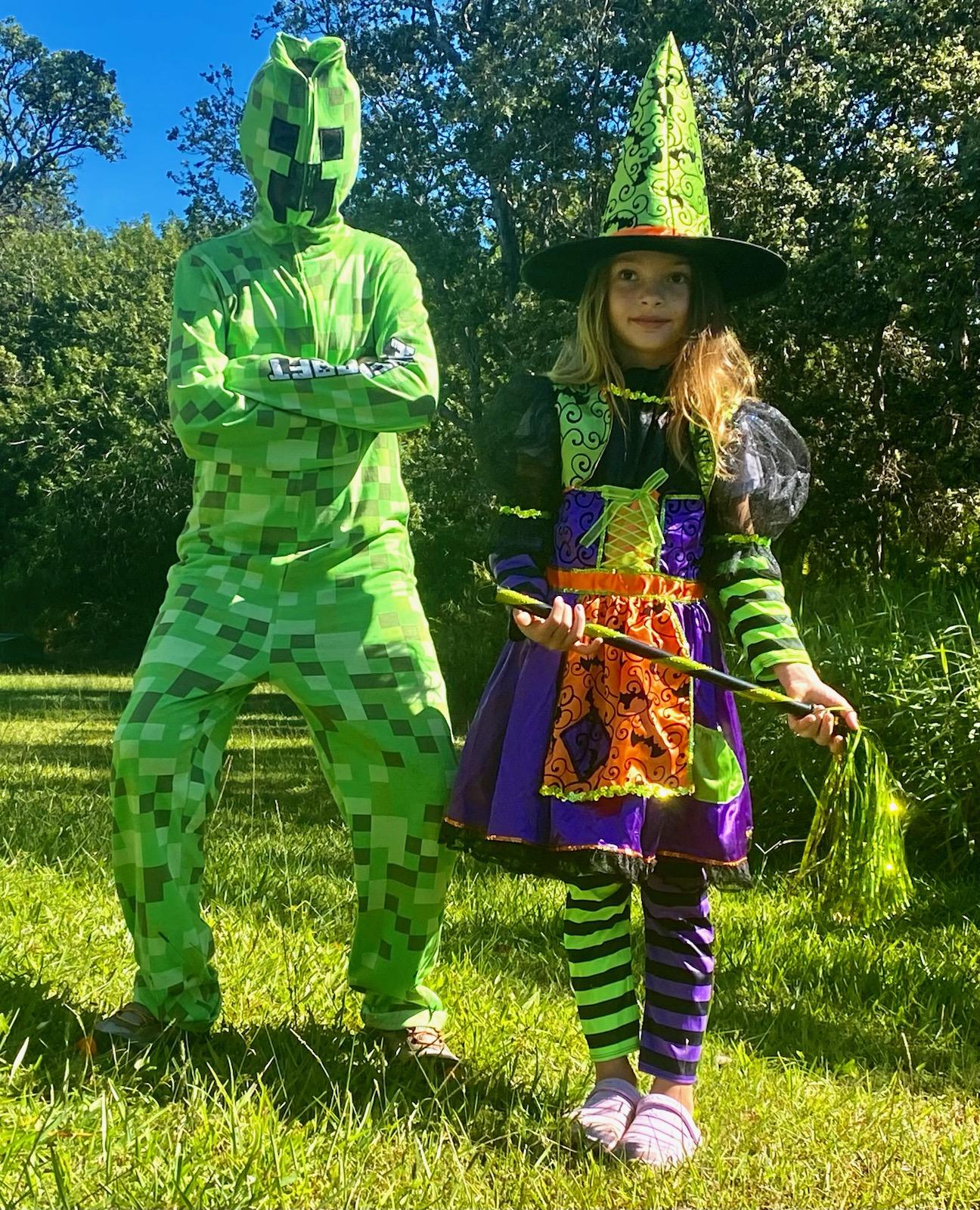 Two costumed children play on a green grass lawn