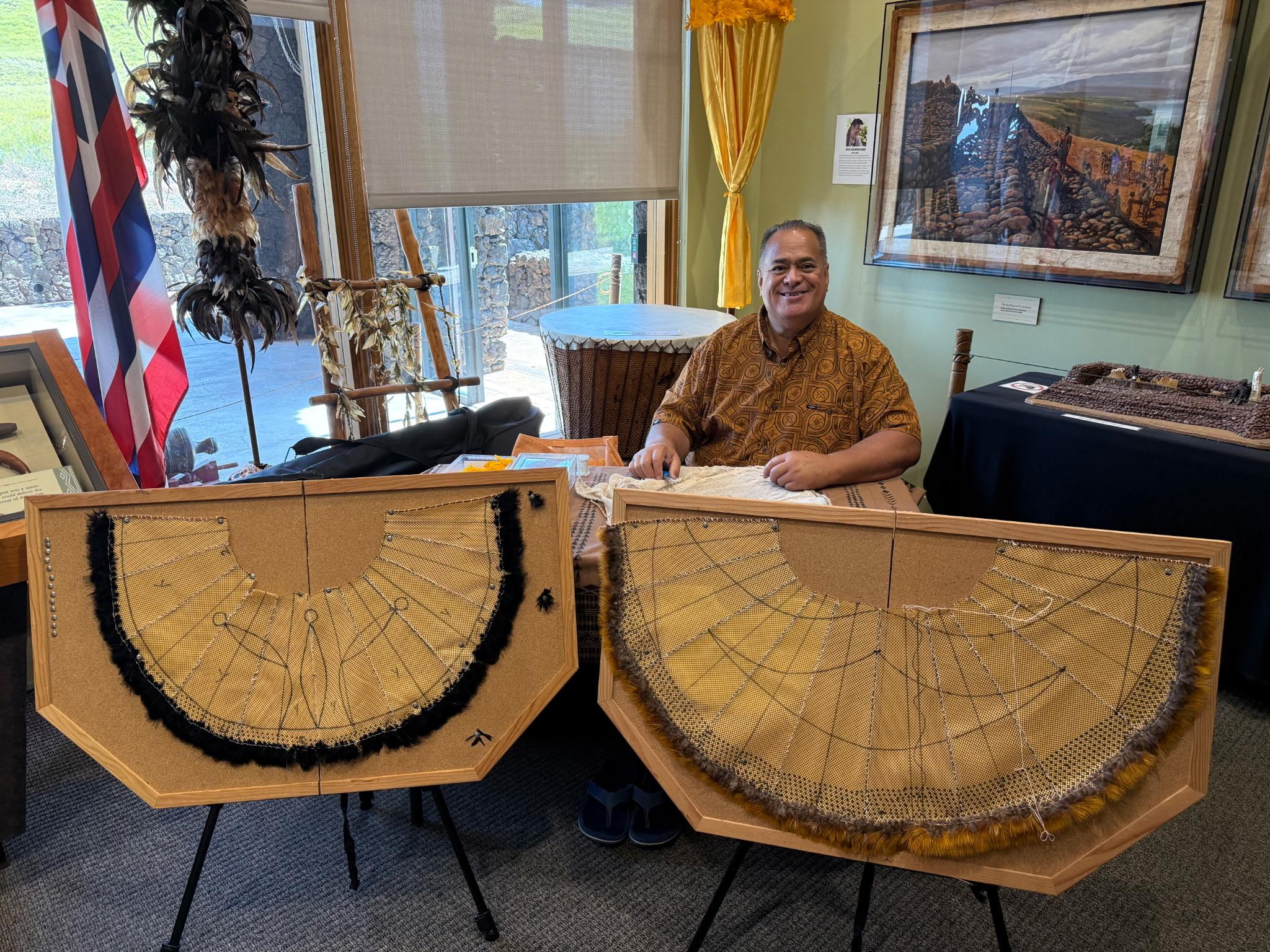 Man seated while working on two traditional Hawaiian capes