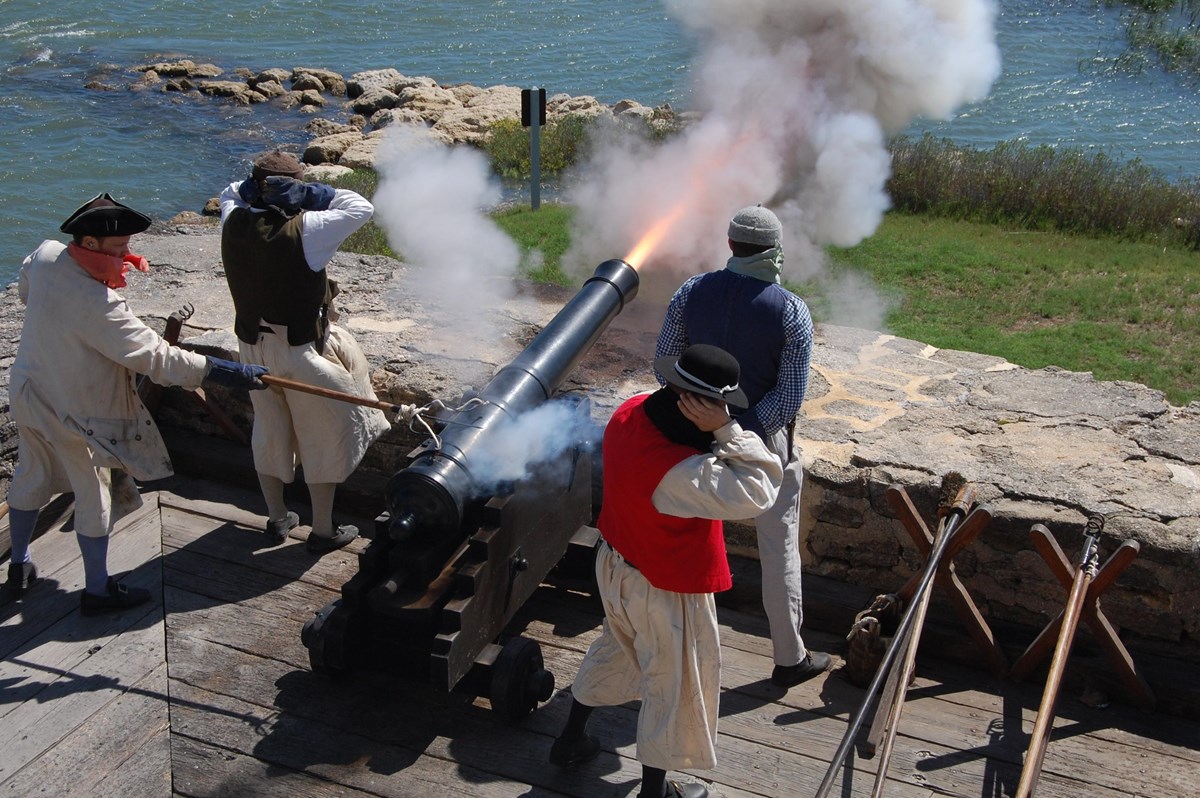 Four people dressed as 18th Century Sailors firing a cannon
