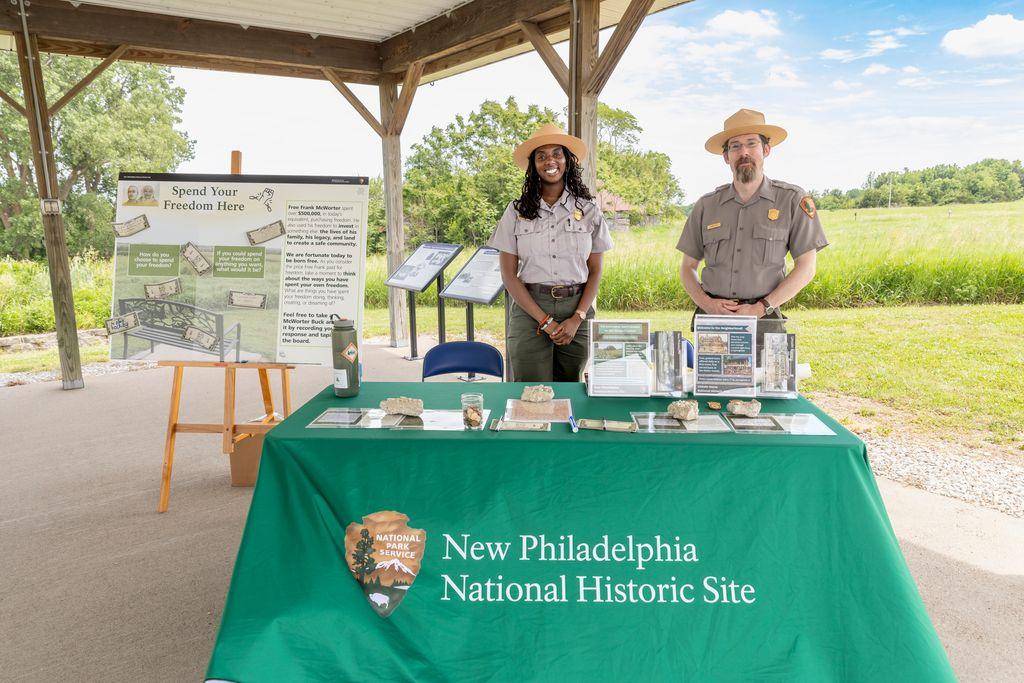 Two park rangers stand behind a table with brochures and a writing prompt activity.