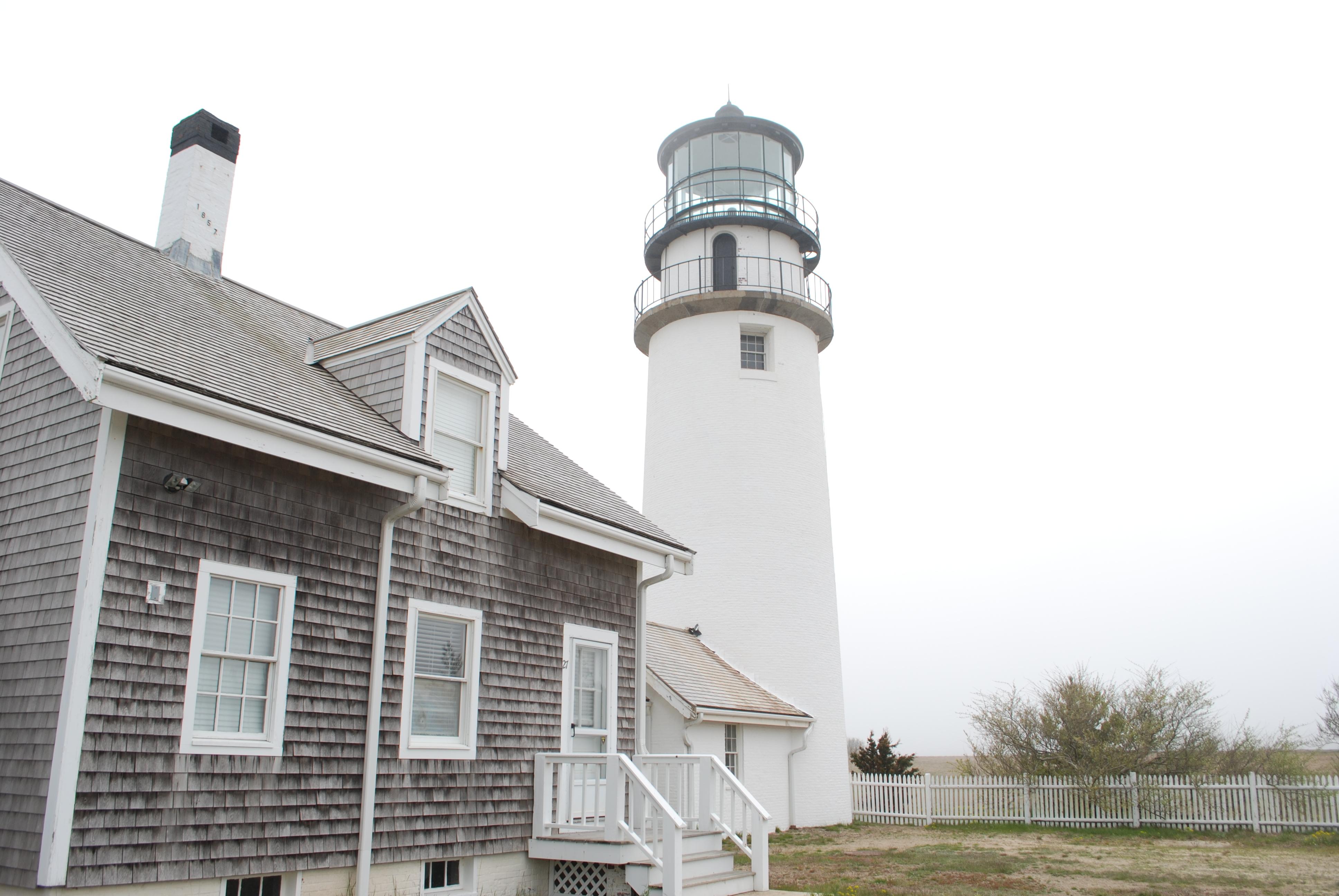 A shingled building next to a tall, white lighthouse.