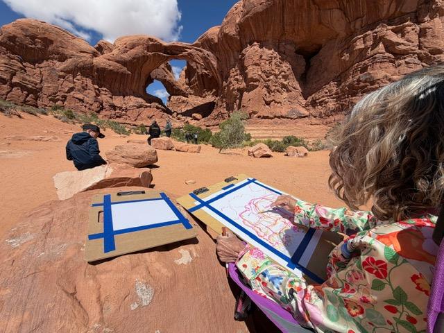 person seated near tall stone openings sketches them onto paper