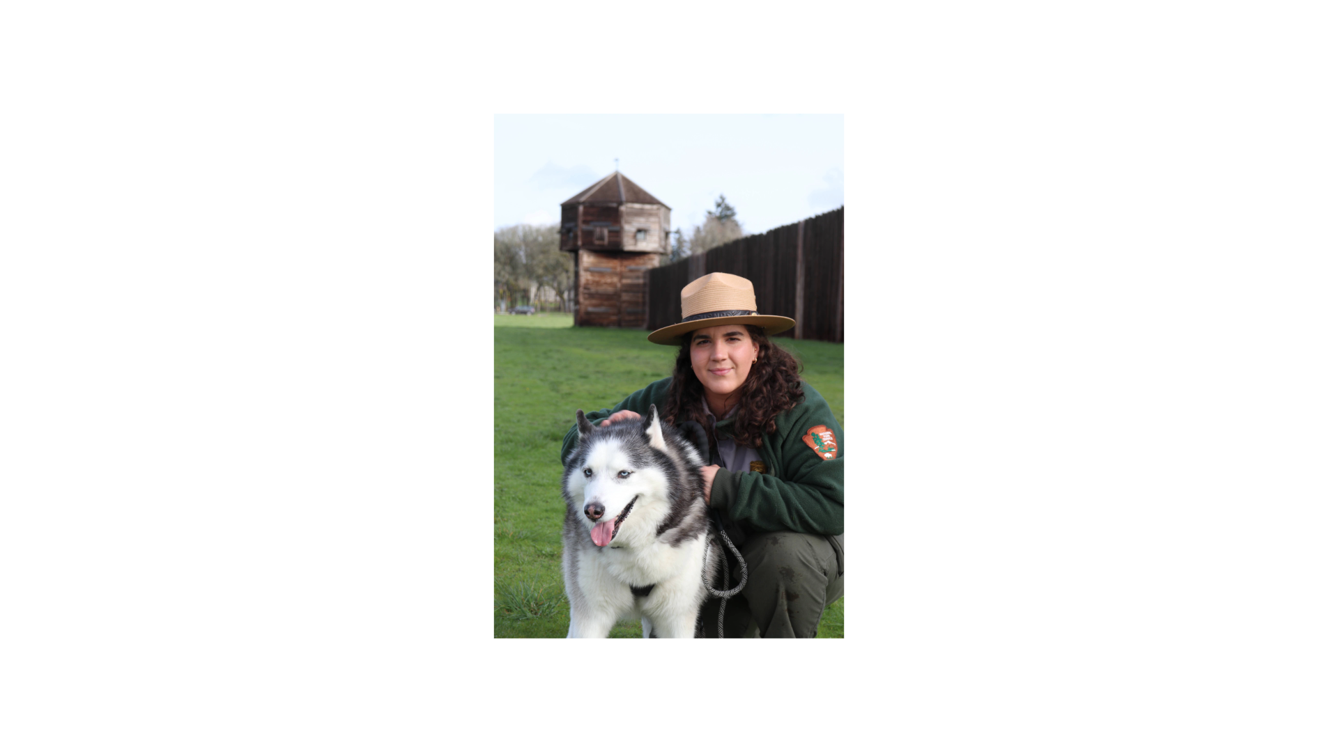 Park Ranger kneeling in front of fort bastion alongside of white and grey Huskey