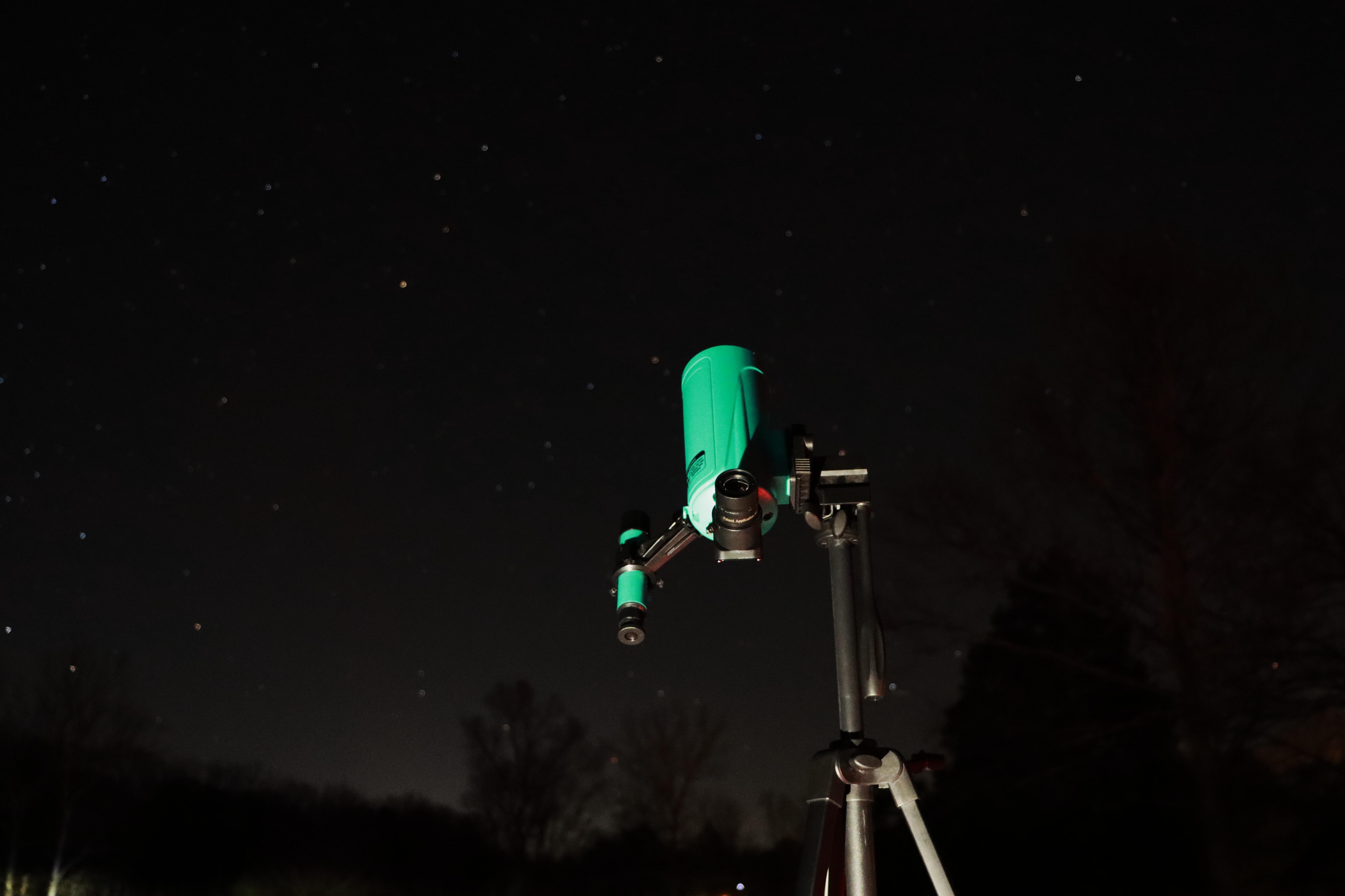 A green telescope aimed at the starry night sky.