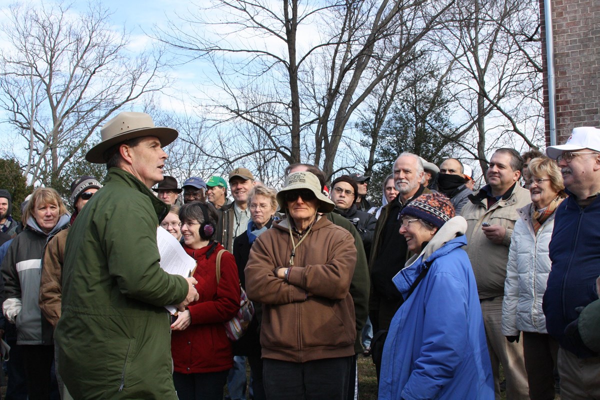 A park ranger speaking outdoors to a large crowd.