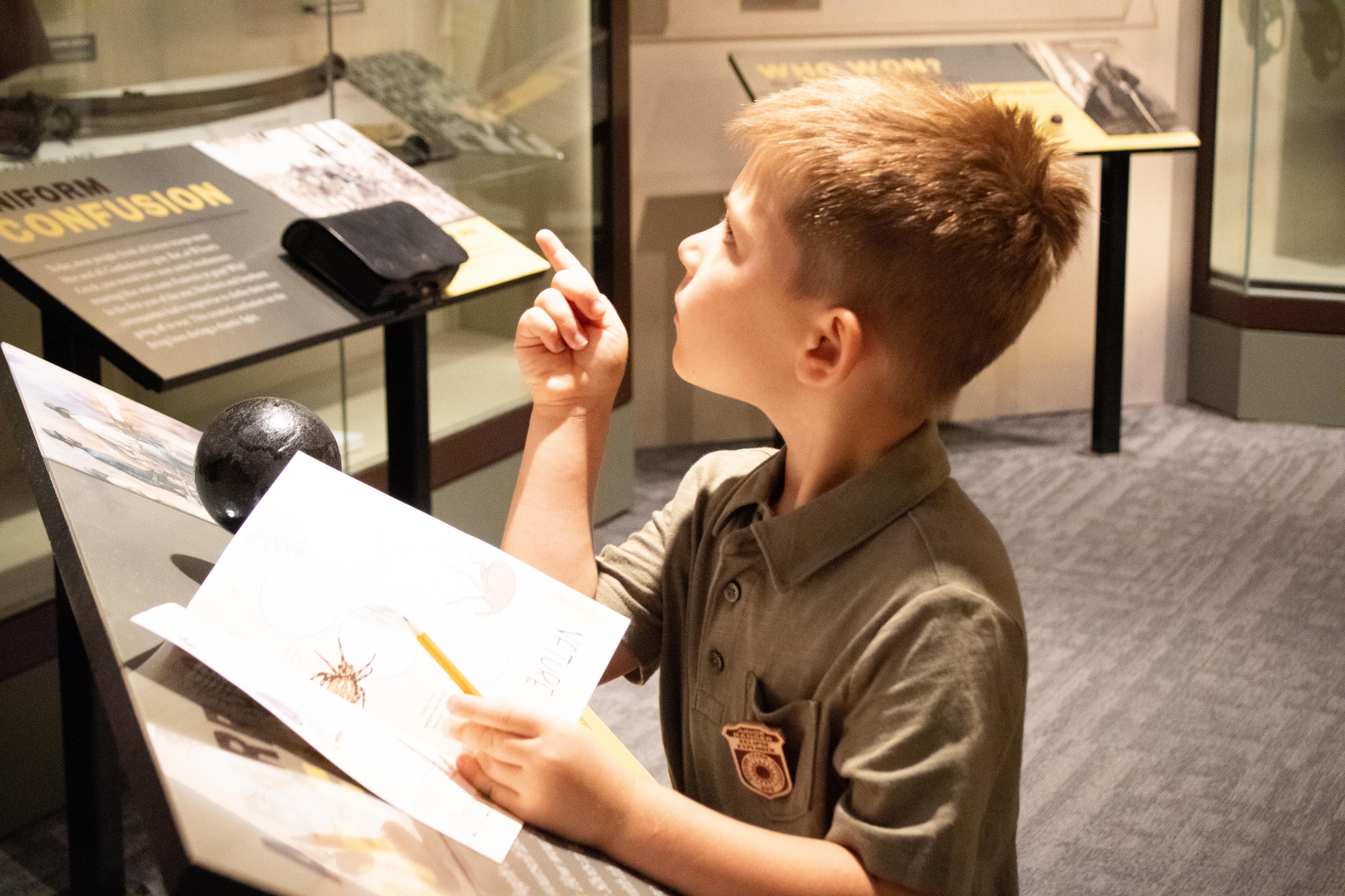 A young boy works on a booklet while looking at a museum display
