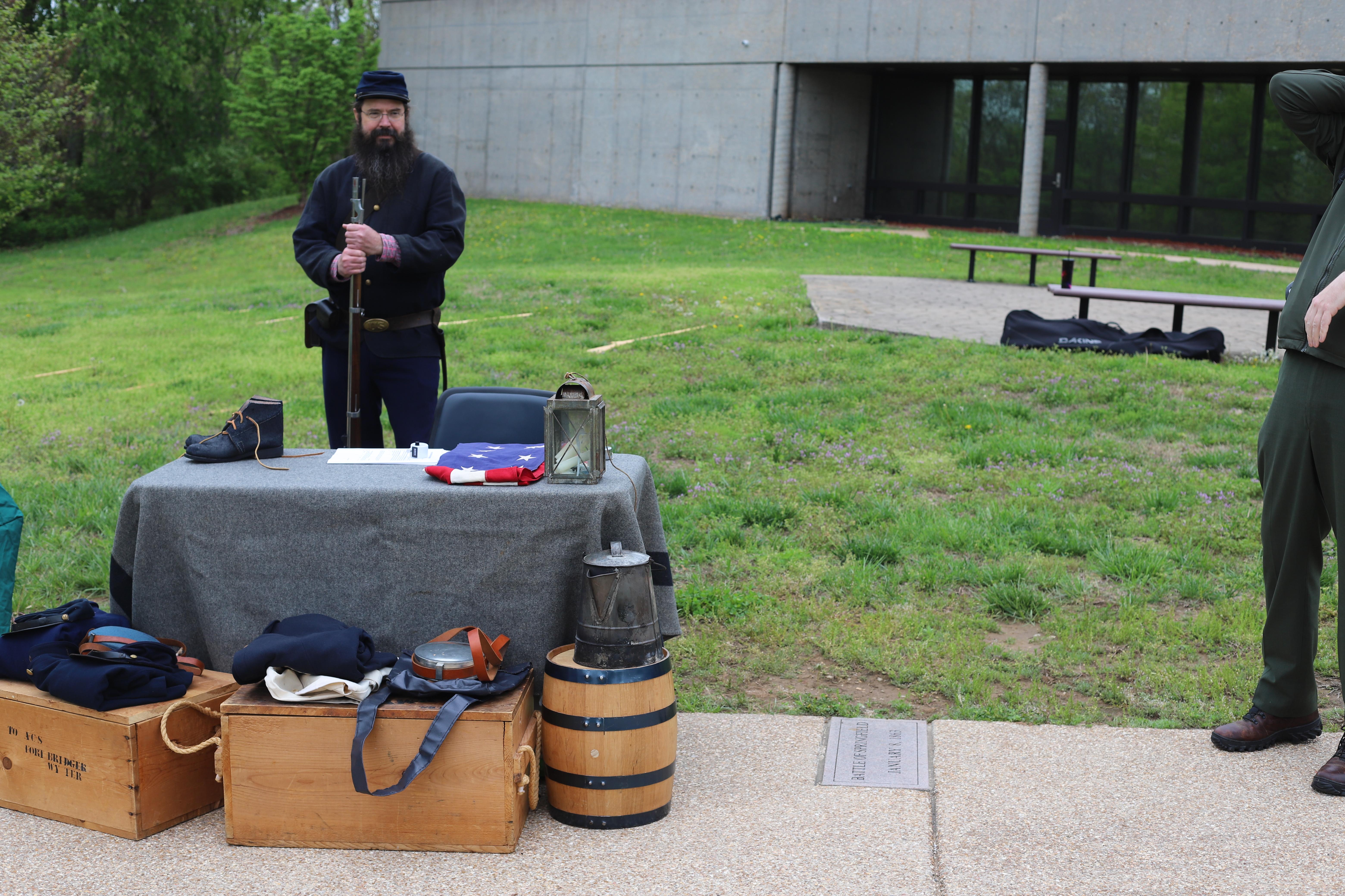 A man in union uniform holding a musket stands behind a table