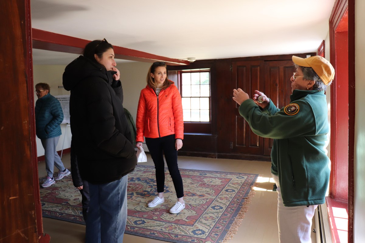 A park volunteer stands inside an 18th century room speaking with multiple visitors