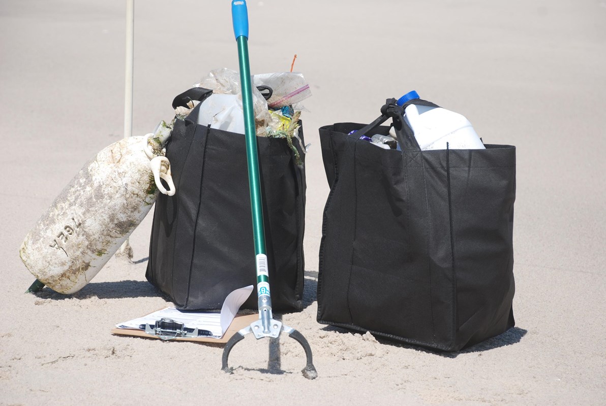 A trash picker and two bags filled with debris rest on a sandy beach.