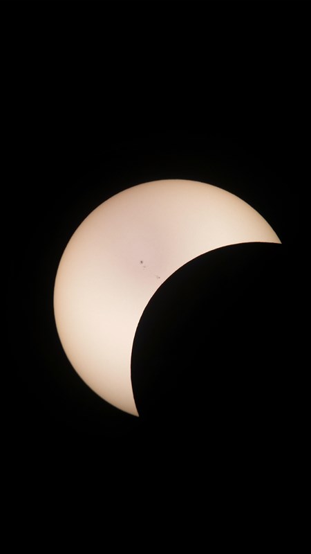 Image of the sun being eclipsed by the moon, making the sun into a crescent shape.