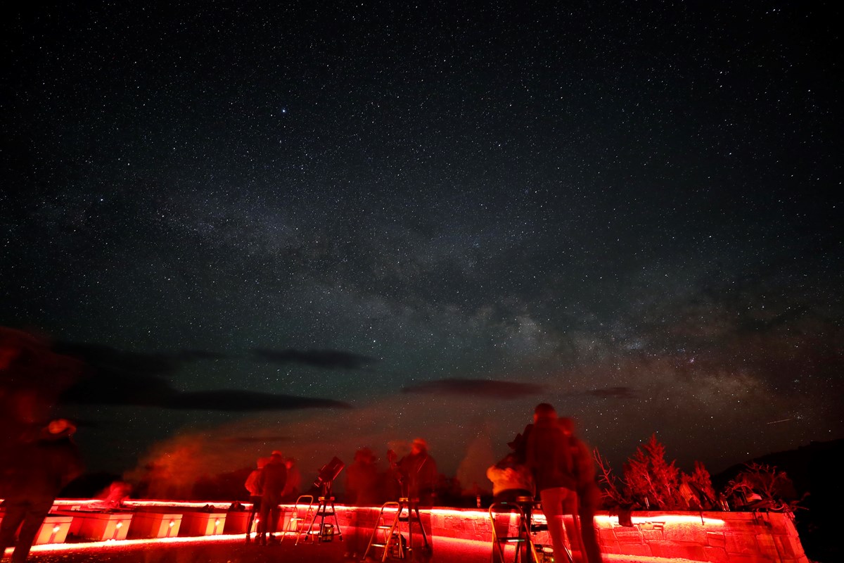 People lit by red lights stand in front of the Milky Way