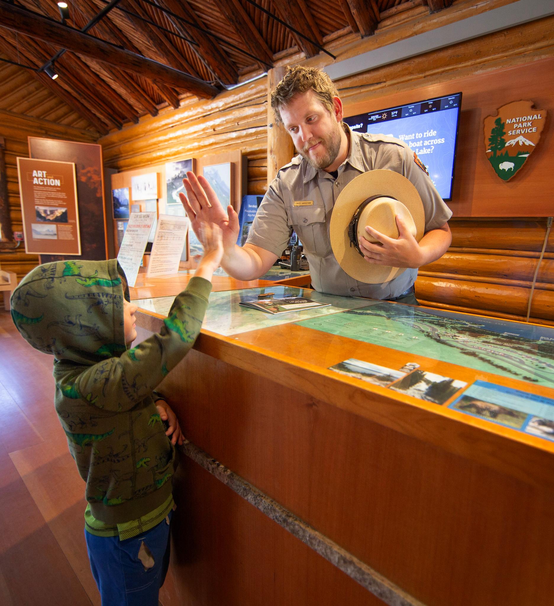 A park ranger gives a child a high five in a visitor center.