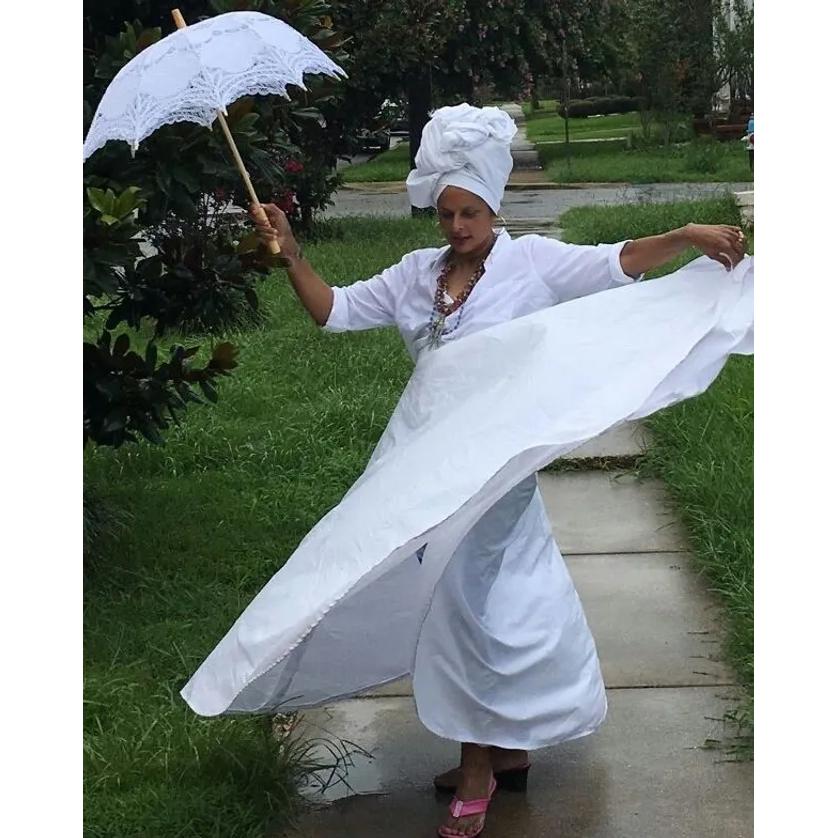 Dianne Honore, dressed in white and holding a white parasol, dances on a sidewalk