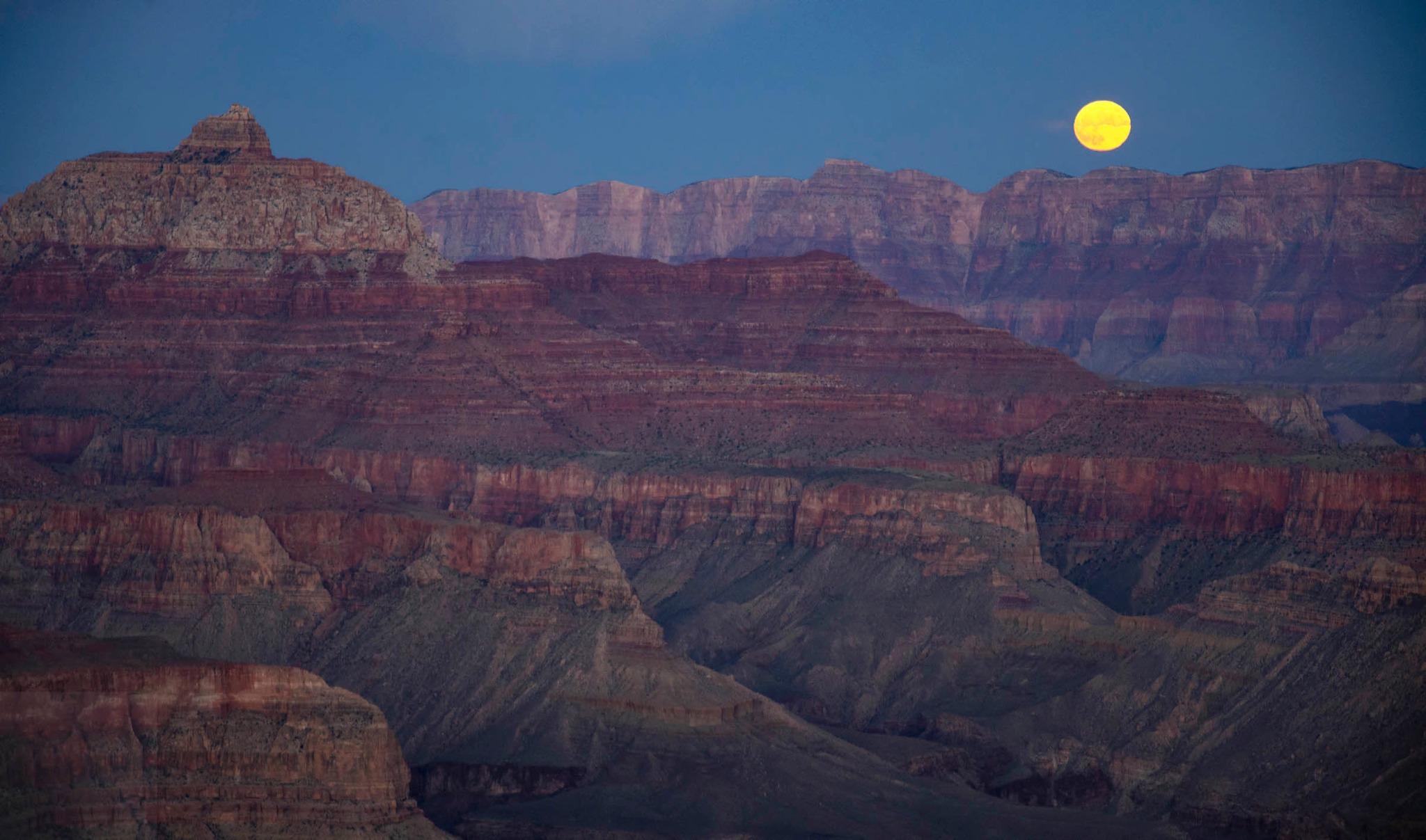 A yellow moon hovering over a canyon landscape