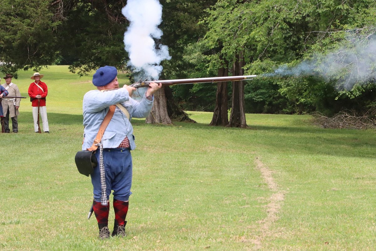 Living historian in Revolutionary War uniform fires a flintlock musket.