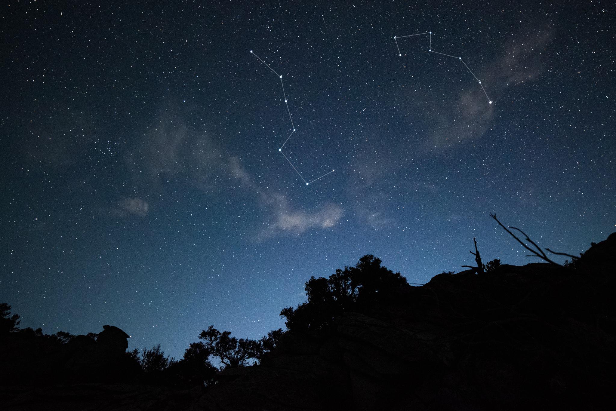 Star filled sky over black silhouetted horizon, big dipper and little dipper outlined and enhanced