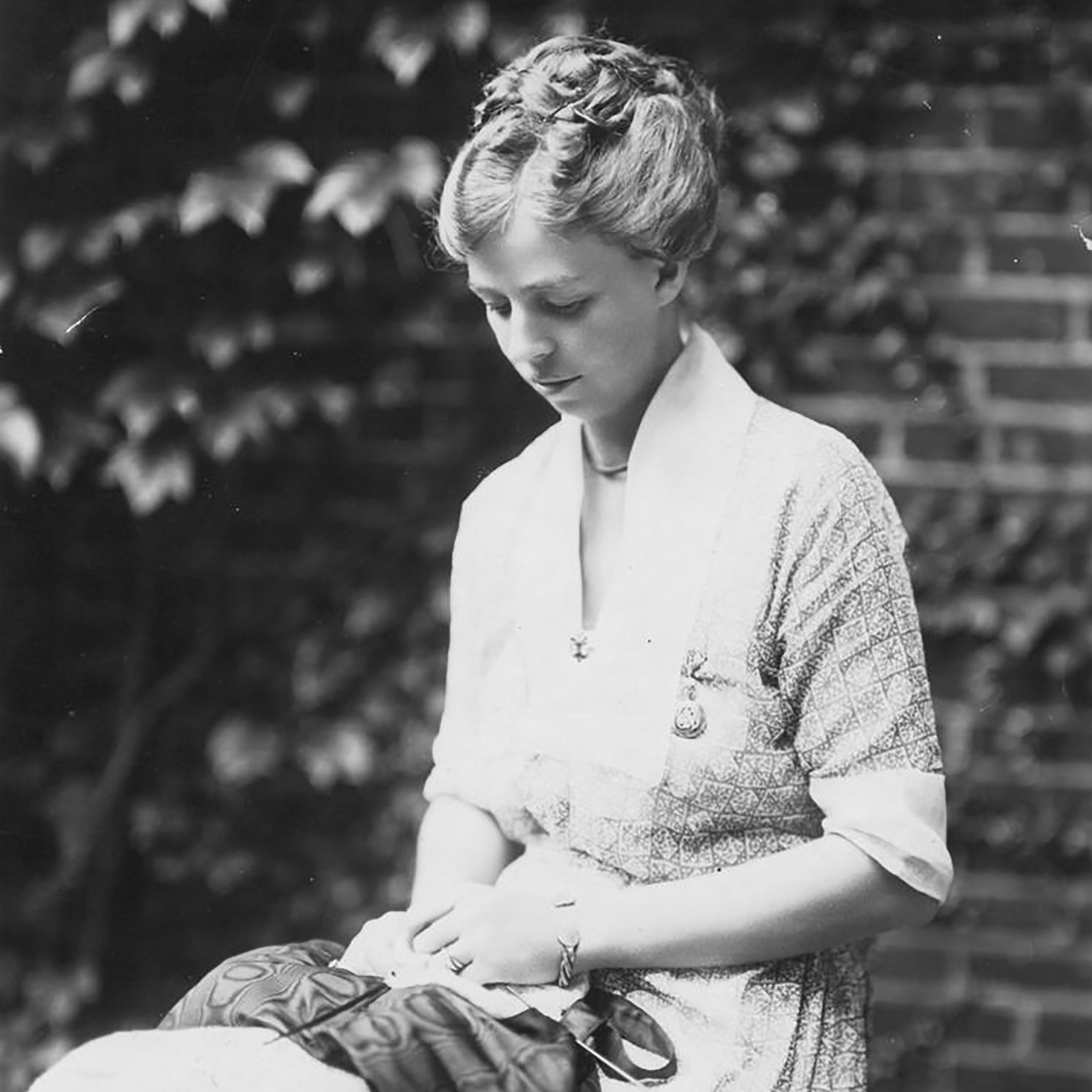 Eleanor Roosevelt sits and looks down at the knitting needle and fabric in her hands.