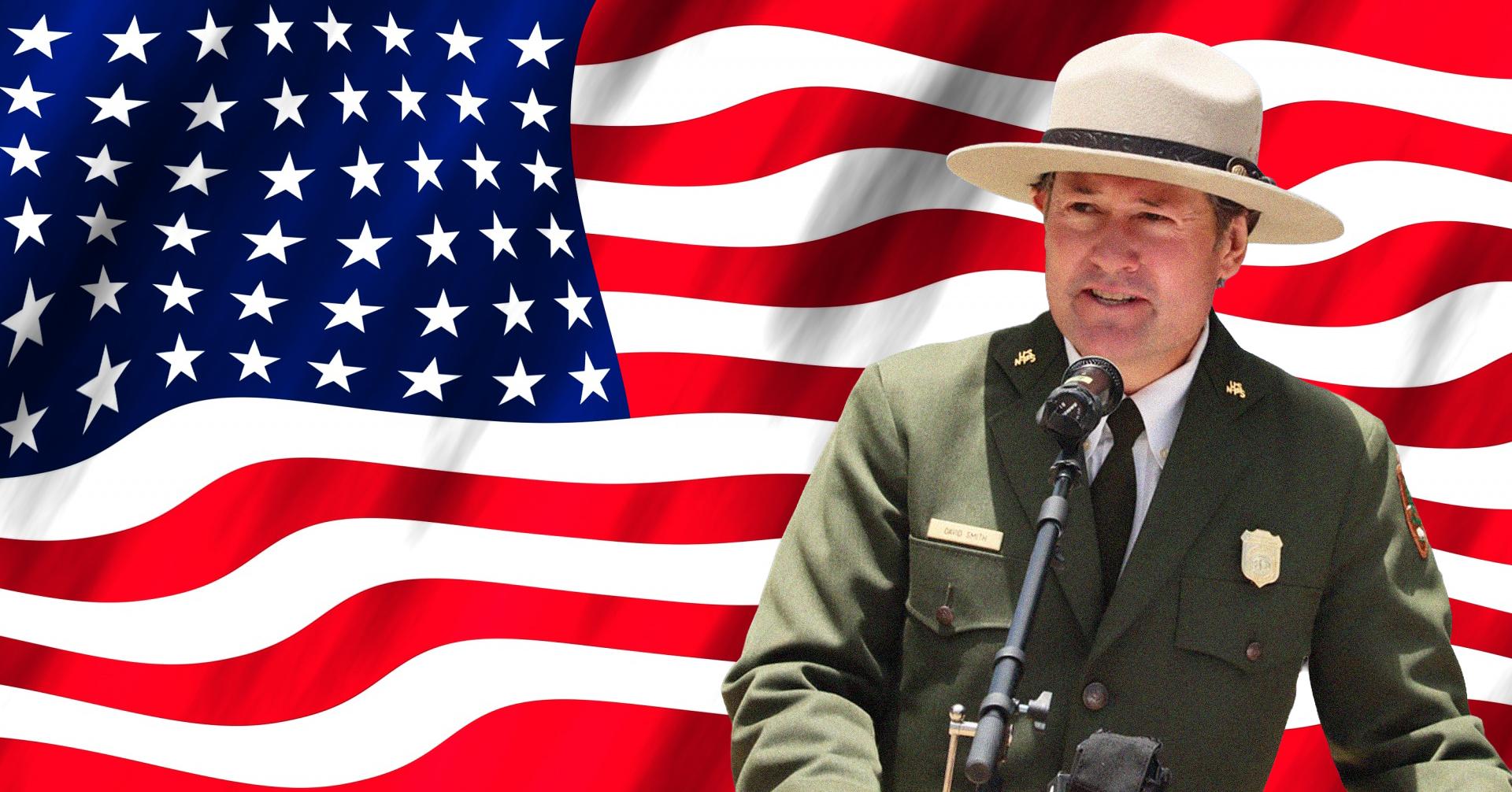 A ranger in uniform stands in front of a microphone with an american flag in the background