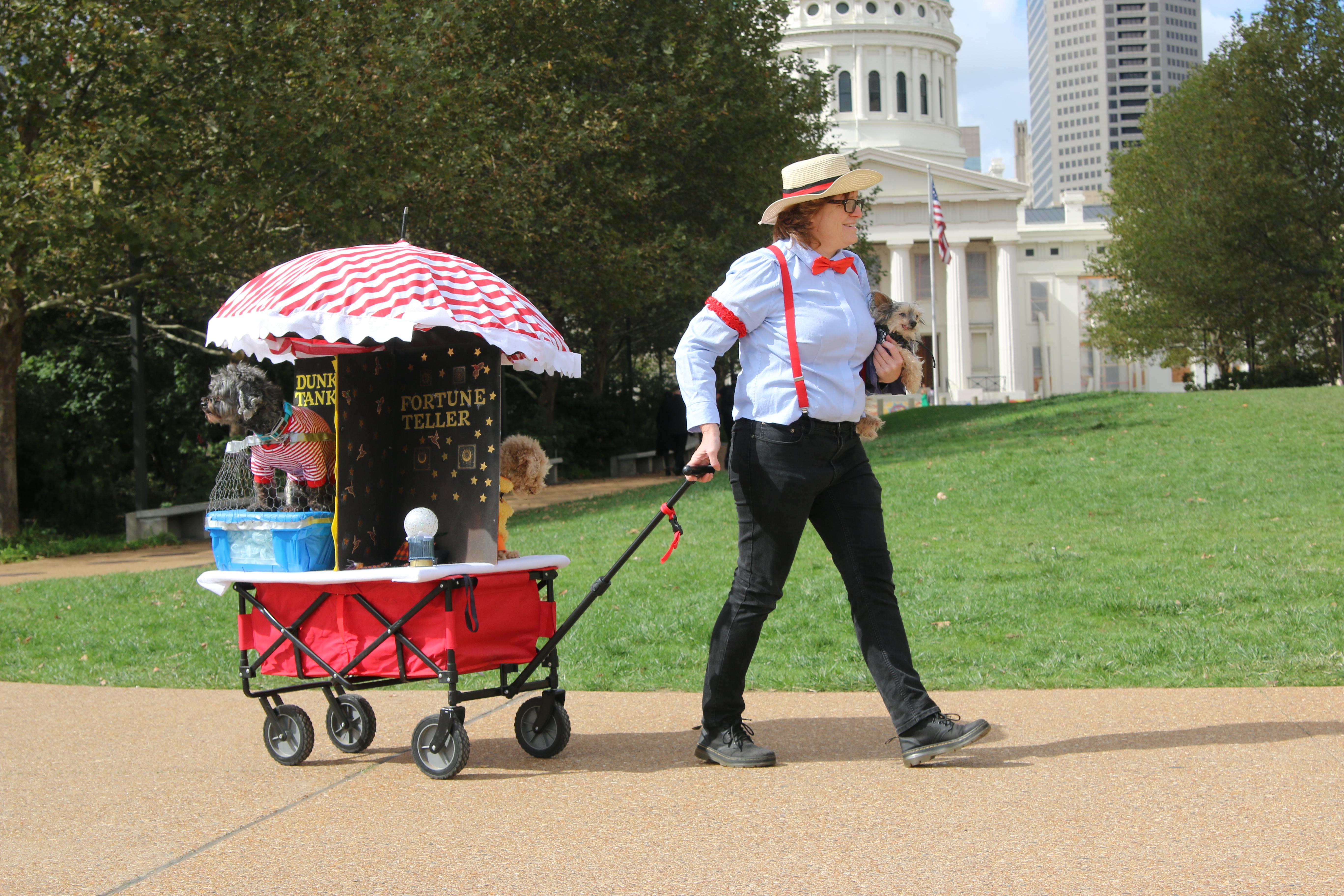 A woman dressed as a ringleader pulls a wagon decorated like a circus tent