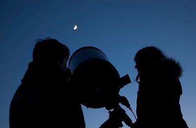 Two people silhoutted by a night sky with a telescope