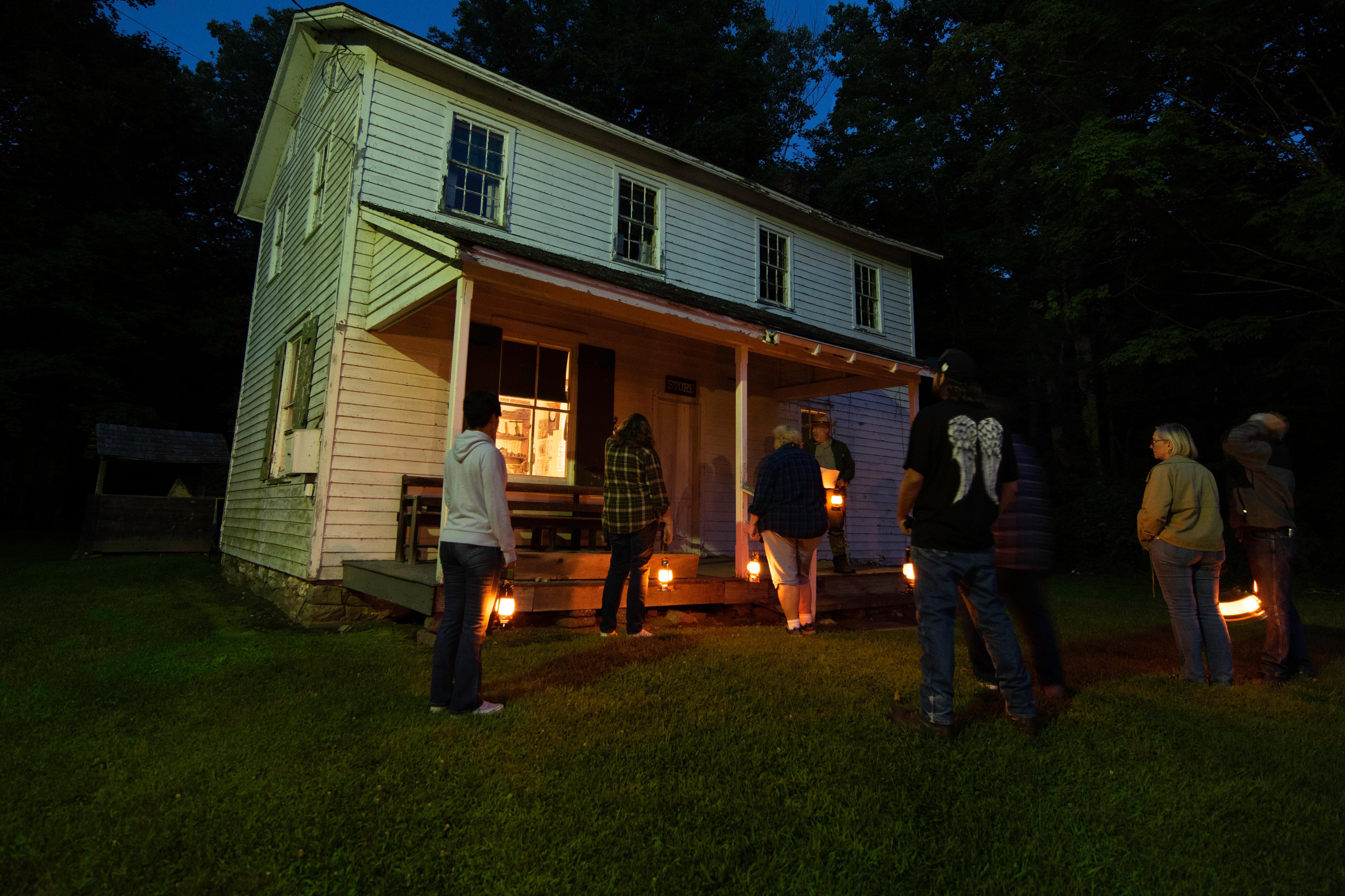 People standing in front of an old building with lanterns and a ranger talking to them.