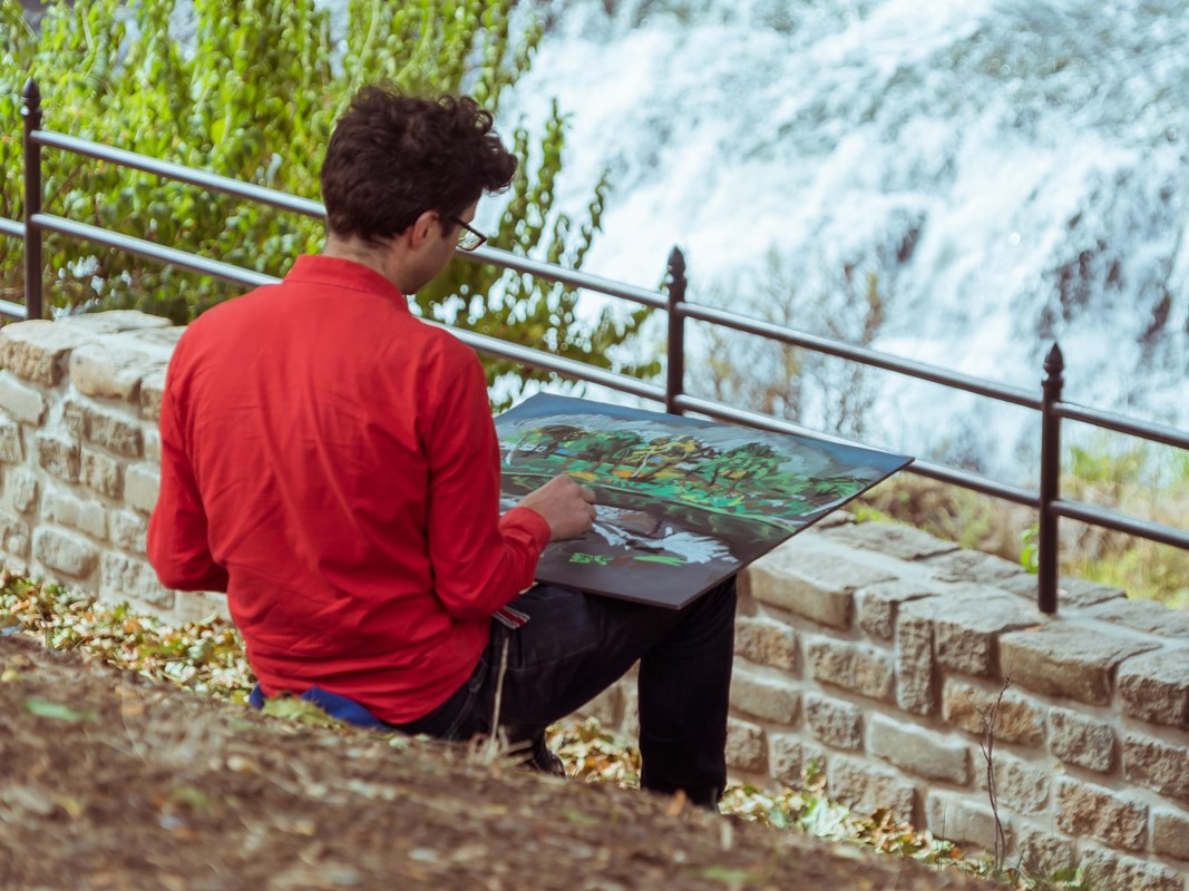 An artist sitting above the waterfall creating a chalk drawing