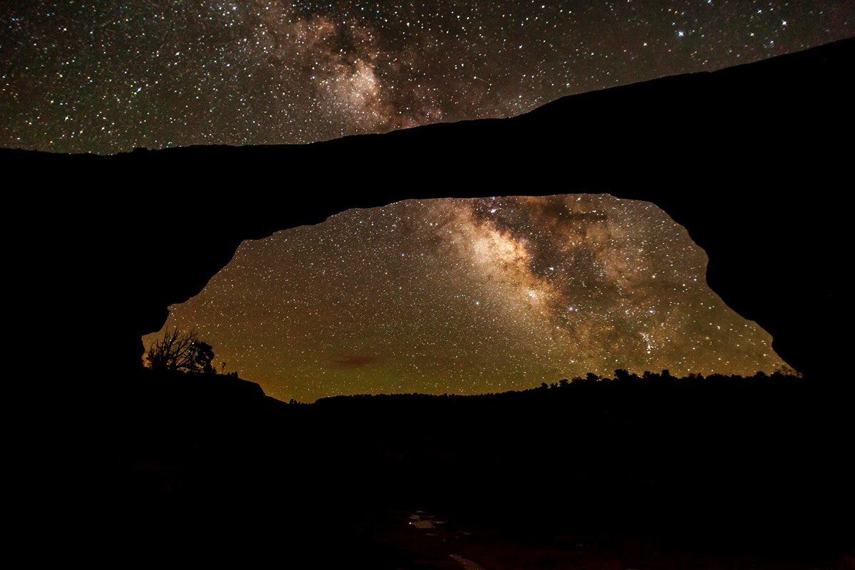 a broad natural stone bridge with the milky way overhead